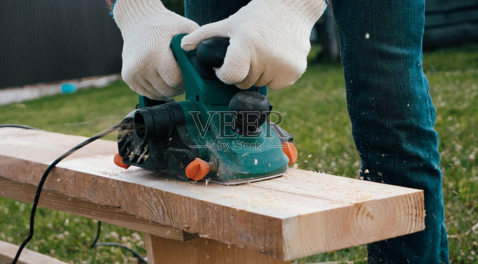 木工手拉手刨刨木材、飞刨花、锯末。戴着手套开电动飞机的特写镜头。使用电动工具工作。照片摄影图片