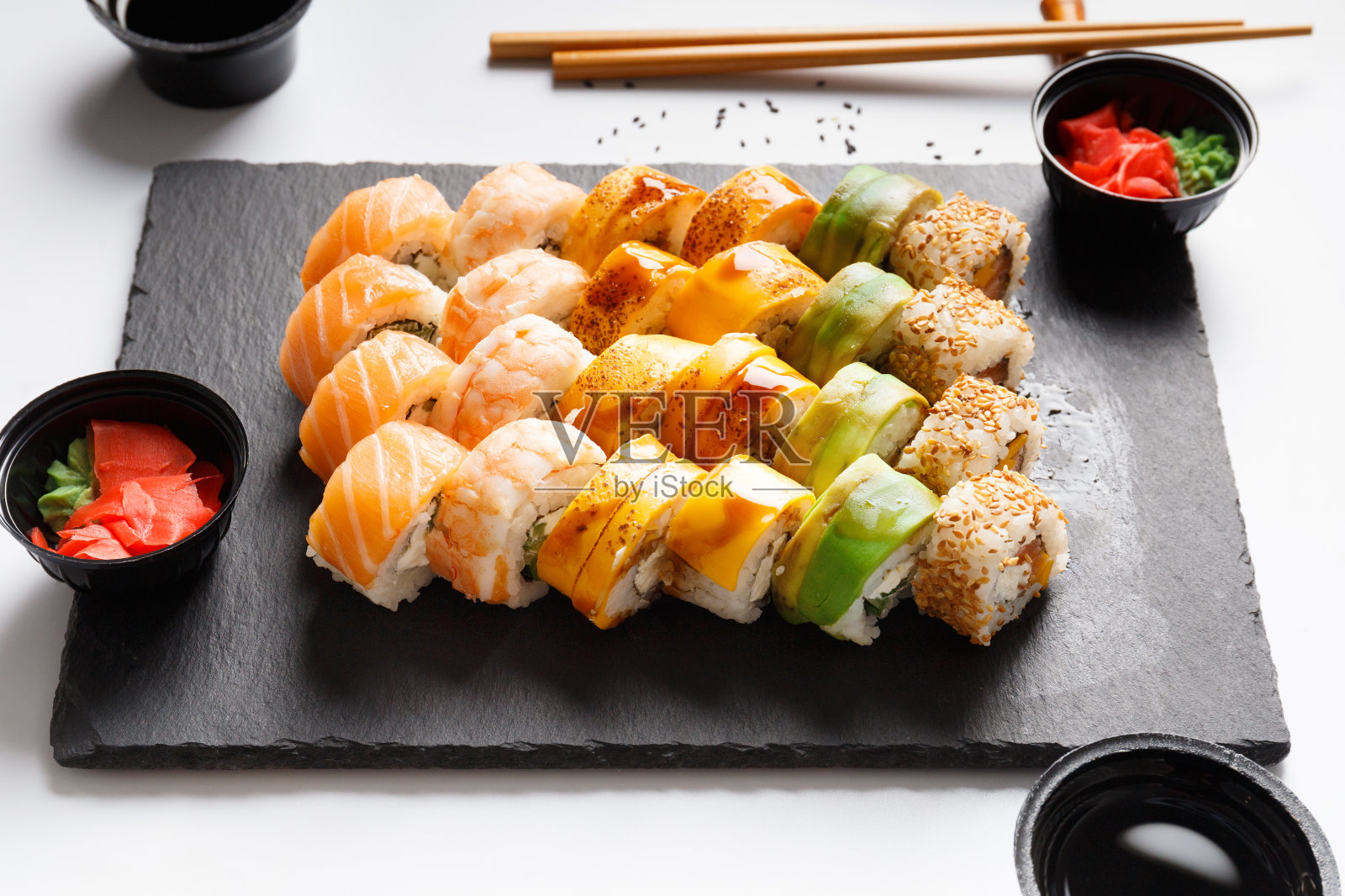 用筷子和灰色背景上的酱油，把各种寿司卷放在石板上照片摄影图片