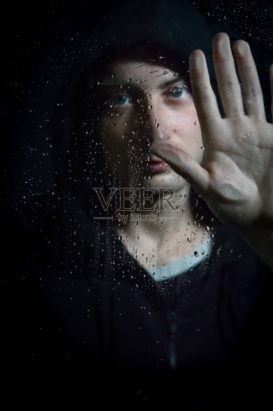 肖像一个年轻的兜帽男子拿着他的手在玻璃上覆盖着水滴-专注于玻璃与水滴和他的手照片摄影图片