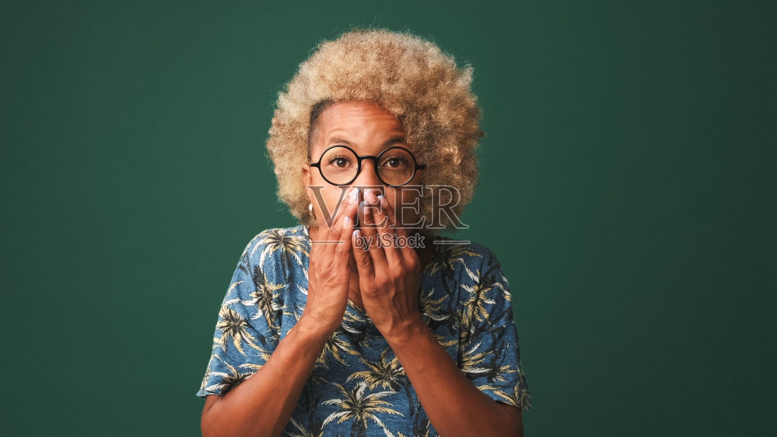 快乐友好的女孩戴着眼镜，穿着一件蓝色的t恤，惊讶地举起双手，用大眼睛看着镜头，震惊，哇效果孤立在绿蓝色的背景下，工作室拍摄照片摄影图片