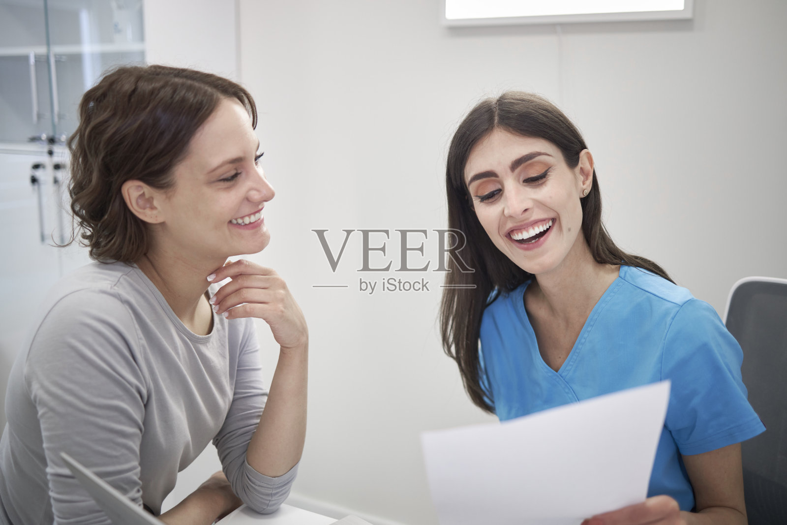 微笑的女医生和快乐的女病人看病历照片摄影图片