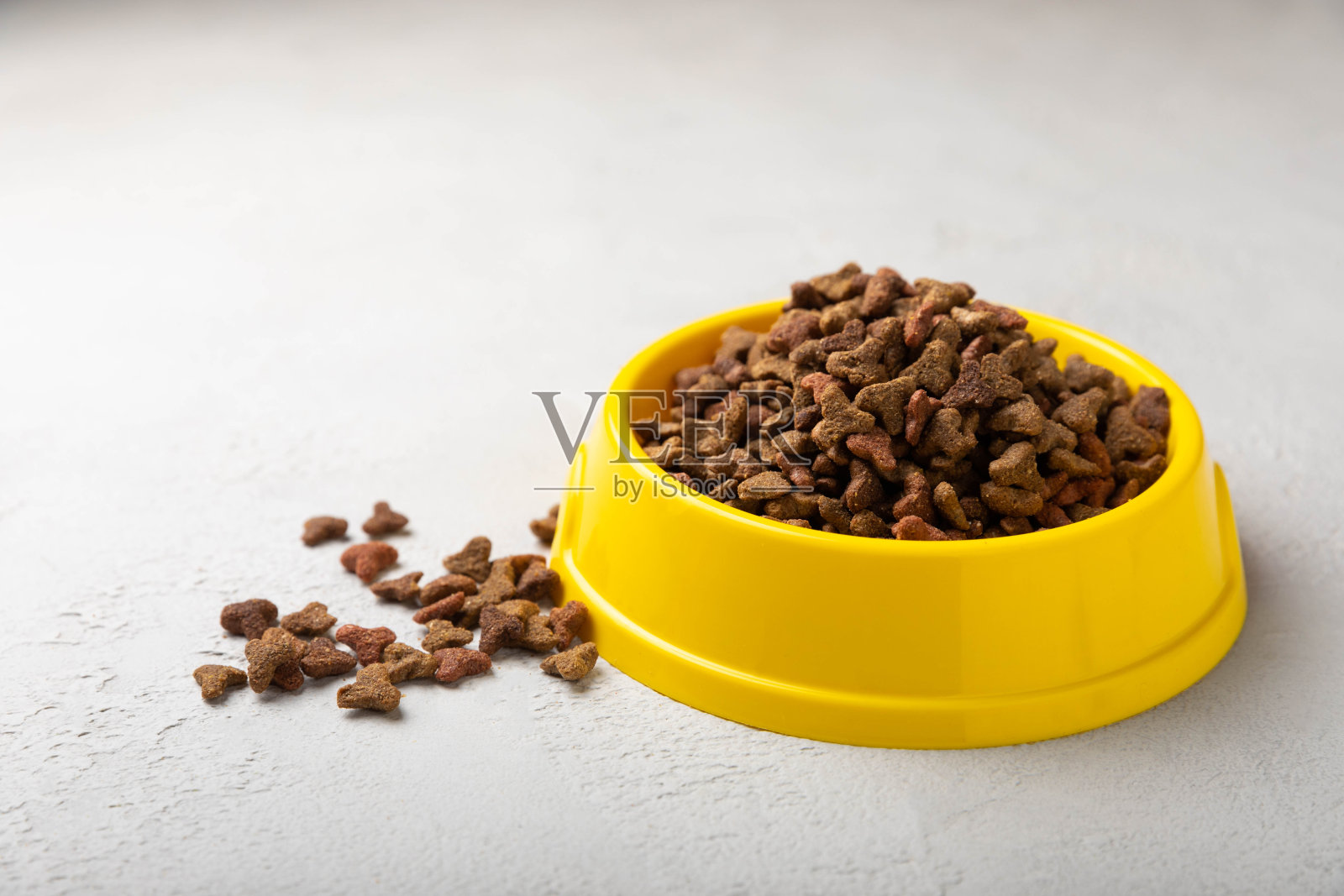 水泥背景上黄色碗里的干猫粮。为宠物提供健康和能量的维生素和营养素。副本的空间。照片摄影图片