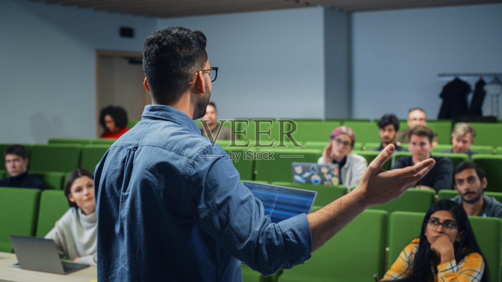 男老师在现代大学教室里给多元的男女学生讲课。好奇和有思想的学者学习和倾听讲师。面向摄像头类照片摄影图片