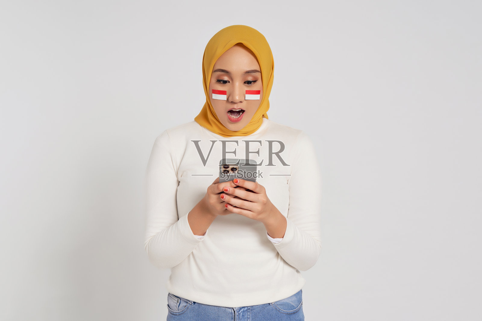 震惊的年轻亚洲穆斯林妇女戴着头巾，在白色背景下用手机阅读新闻。8月17日庆祝印尼独立日照片摄影图片