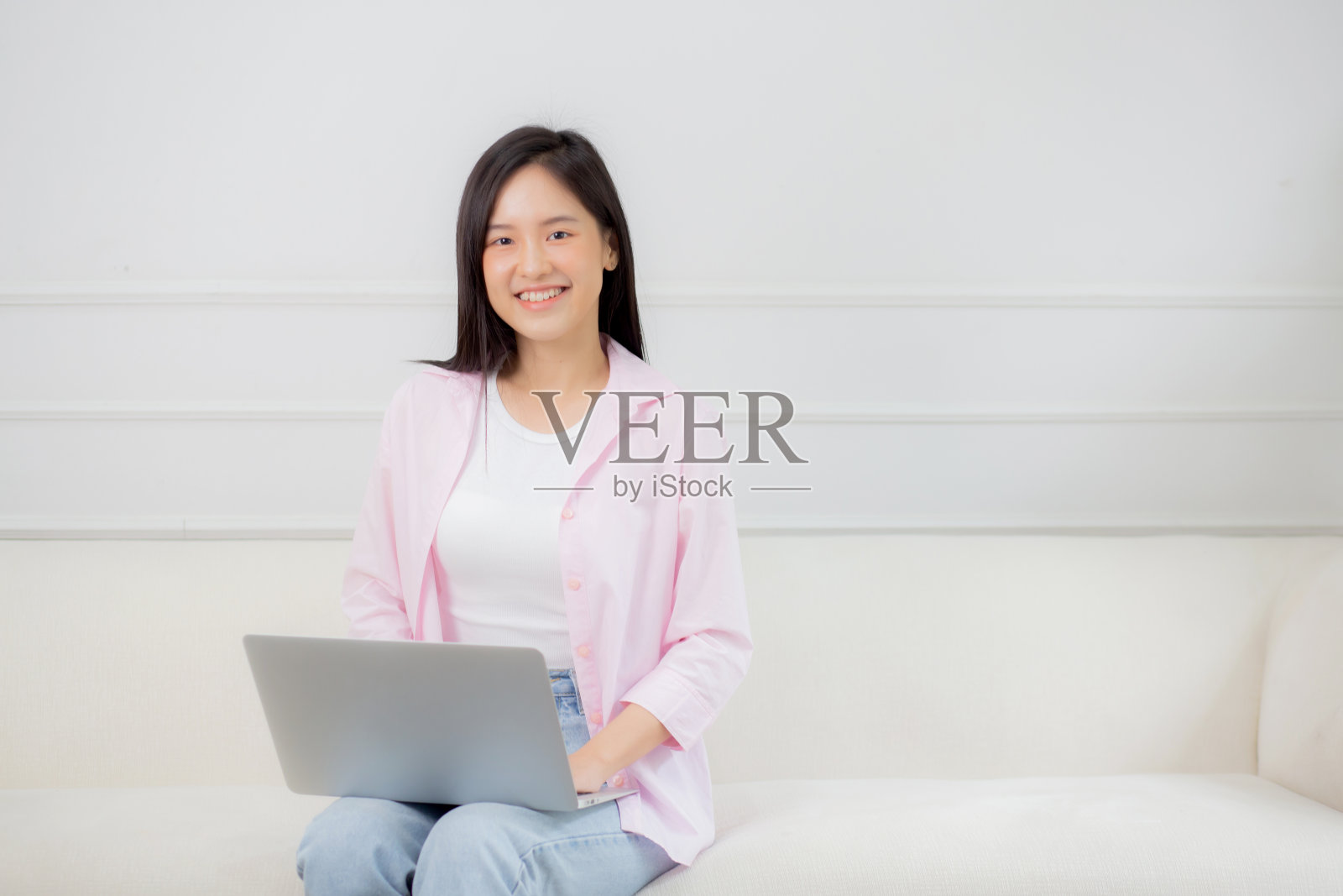 年轻的亚洲商业女性在家里用笔记本电脑在客厅的沙发上上网，自由职业者女孩坐在沙发上用笔记本电脑舒适放松，生活方式的概念。照片摄影图片