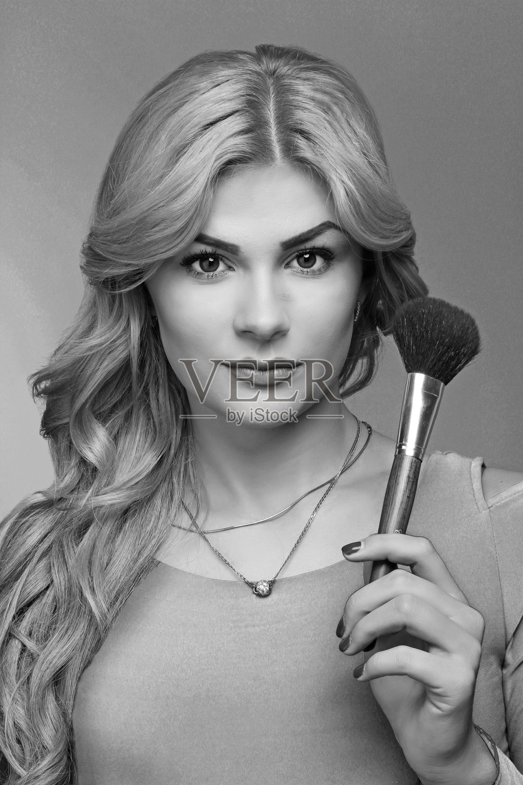 一个金发碧眼的化妆师女孩的肖像，她穿着蓝色的裙子，在工作室里拿着刷脸，化妆和发型，红唇和指甲，画画照片摄影图片