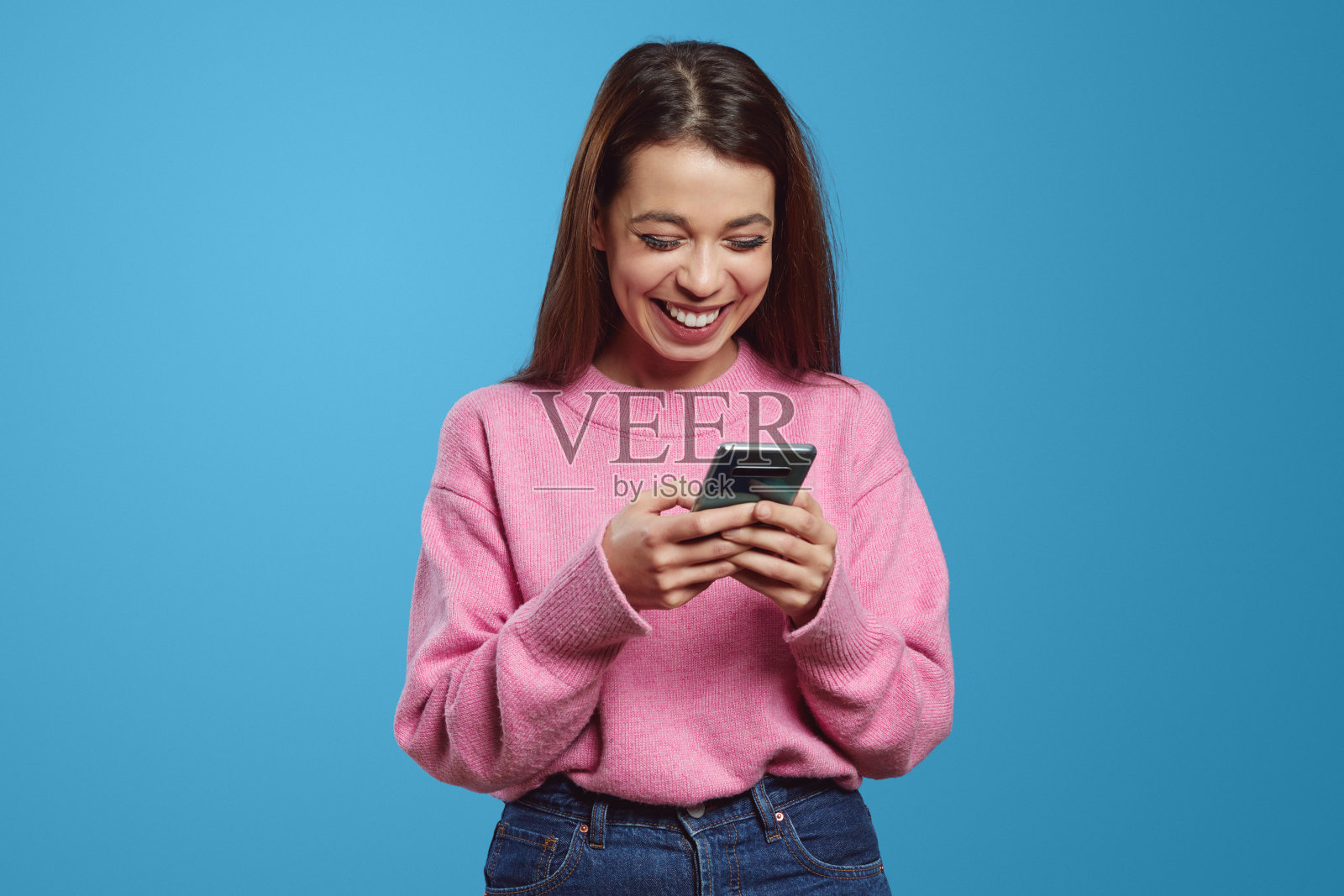 积极向上的年轻西班牙裔千禧一代女性一边用手机发信息一边开心地笑着照片摄影图片