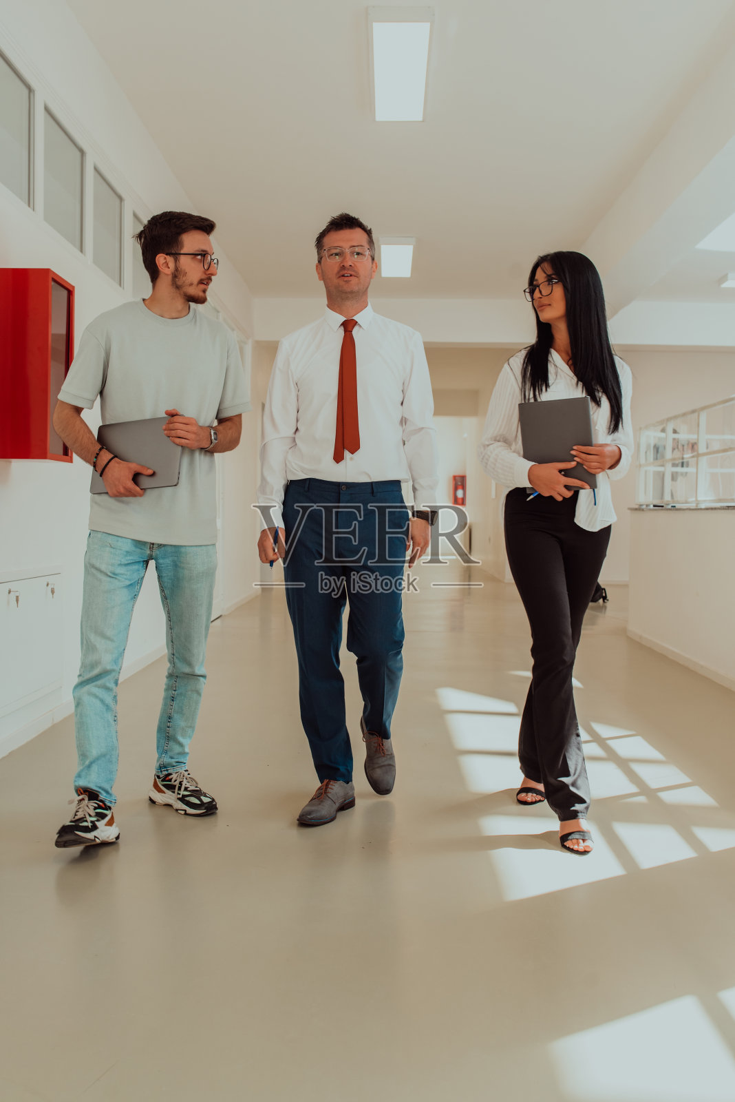 在一家大公司现代化宽敞的走廊里，导演与秘书和一名年轻的程序员交谈，讨论各种商业话题和项目。照片摄影图片