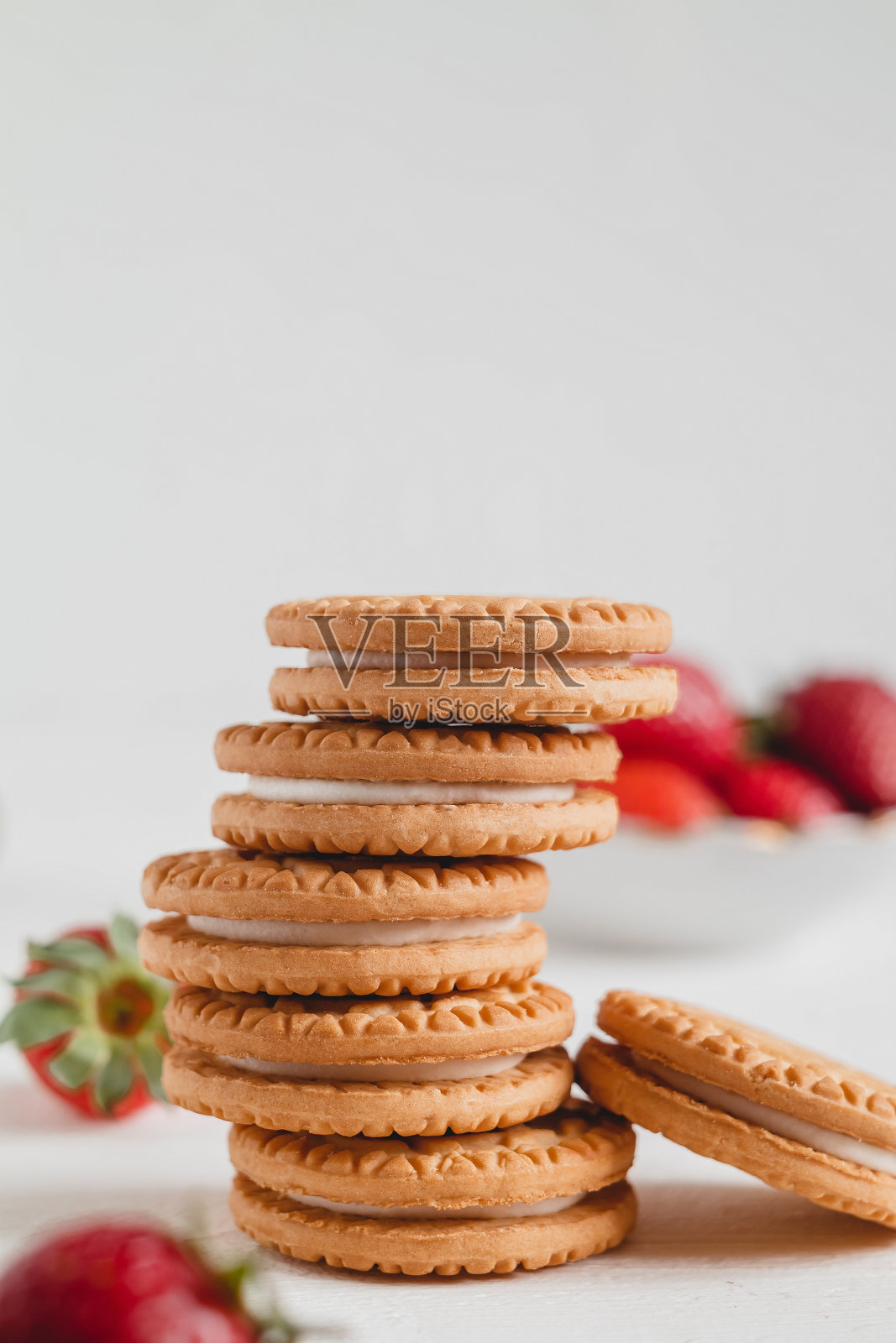 白色的桌子上，一堆甜的三明治饼干和新鲜的红草莓。照片摄影图片