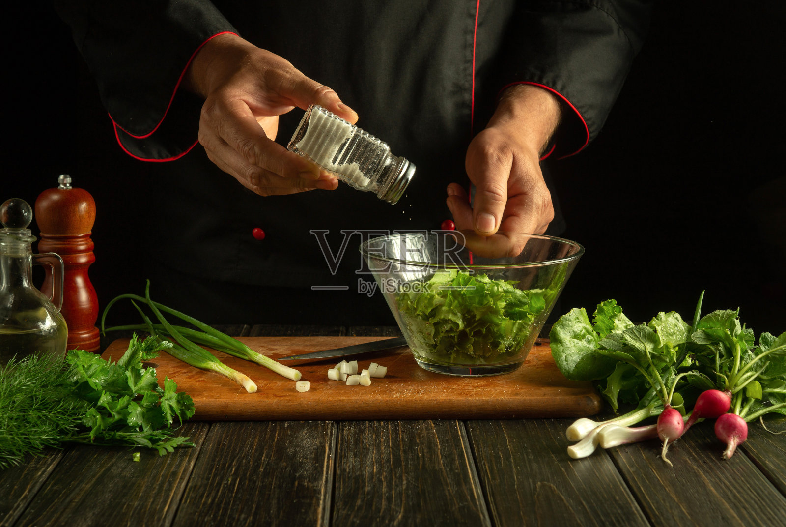 厨师在蔬菜沙拉里加了盐。素食是由厨师在厨房里亲手制作的。酒店或餐厅菜单上的素食点子照片摄影图片