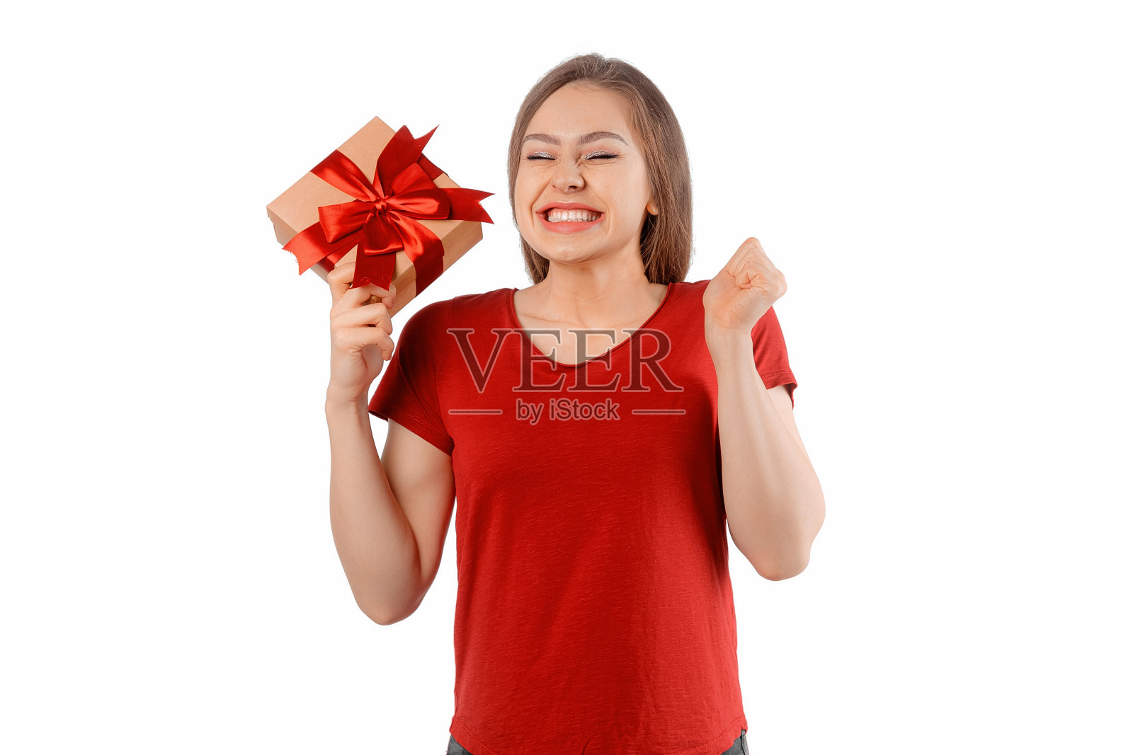 一个穿着红色t恤的快乐微笑的女孩的肖像，拿着礼物盒，在白色背景上摆姿势。开朗的黑发女人长着头发，微笑着，笑着，看起来很高兴照片摄影图片
