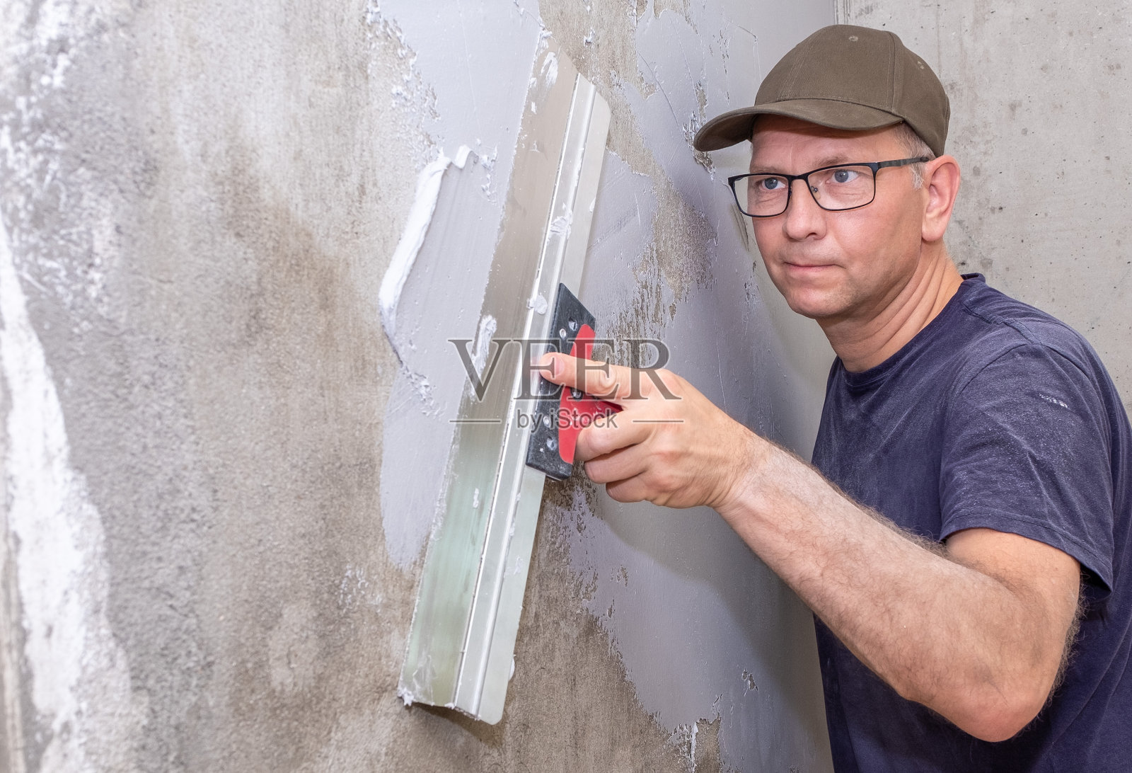 建筑工人是一个白人，他用施工抹子把腻子涂在墙上。照片摄影图片