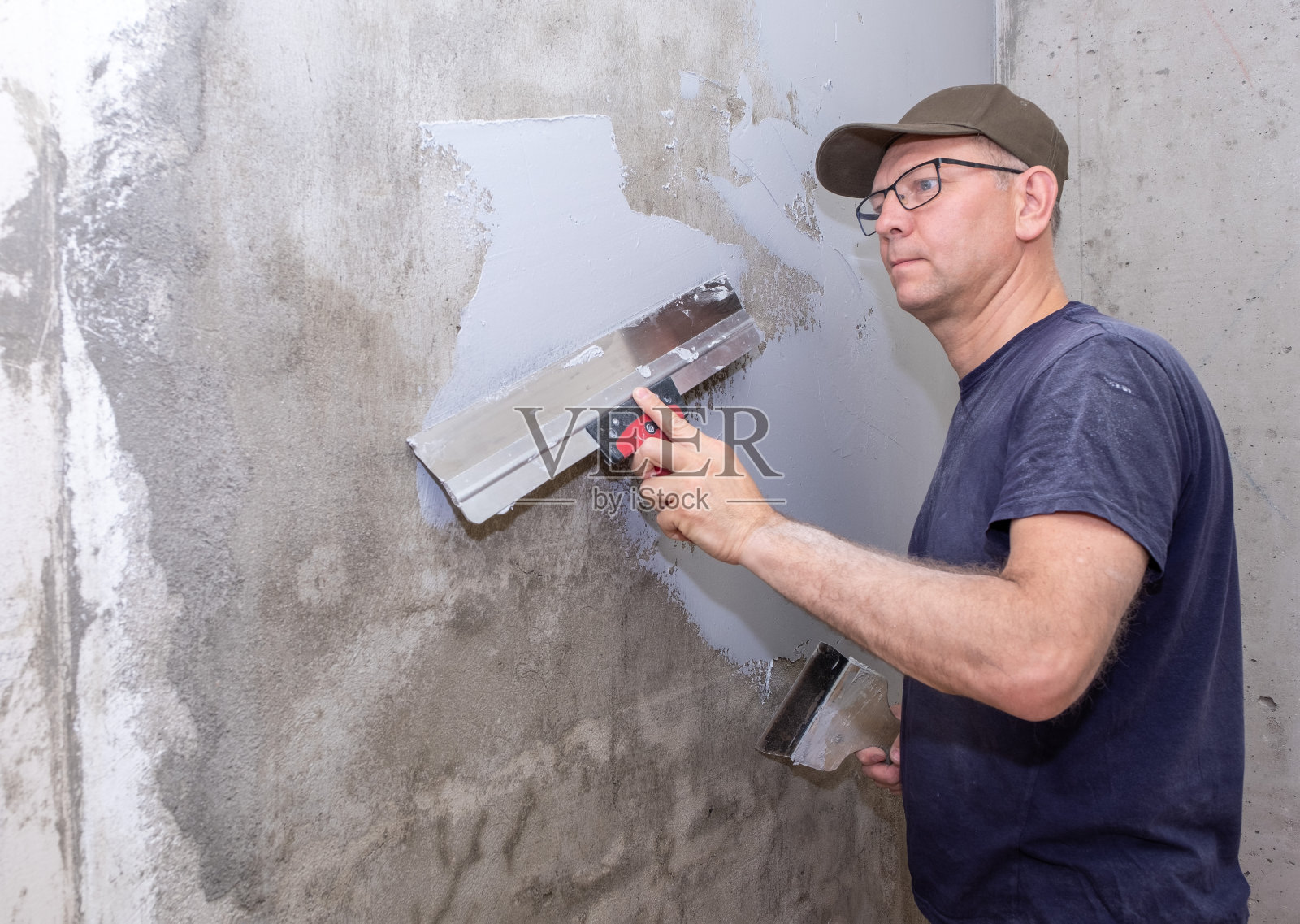 建筑工人是一个白人，他用施工抹子把腻子涂在墙上。照片摄影图片