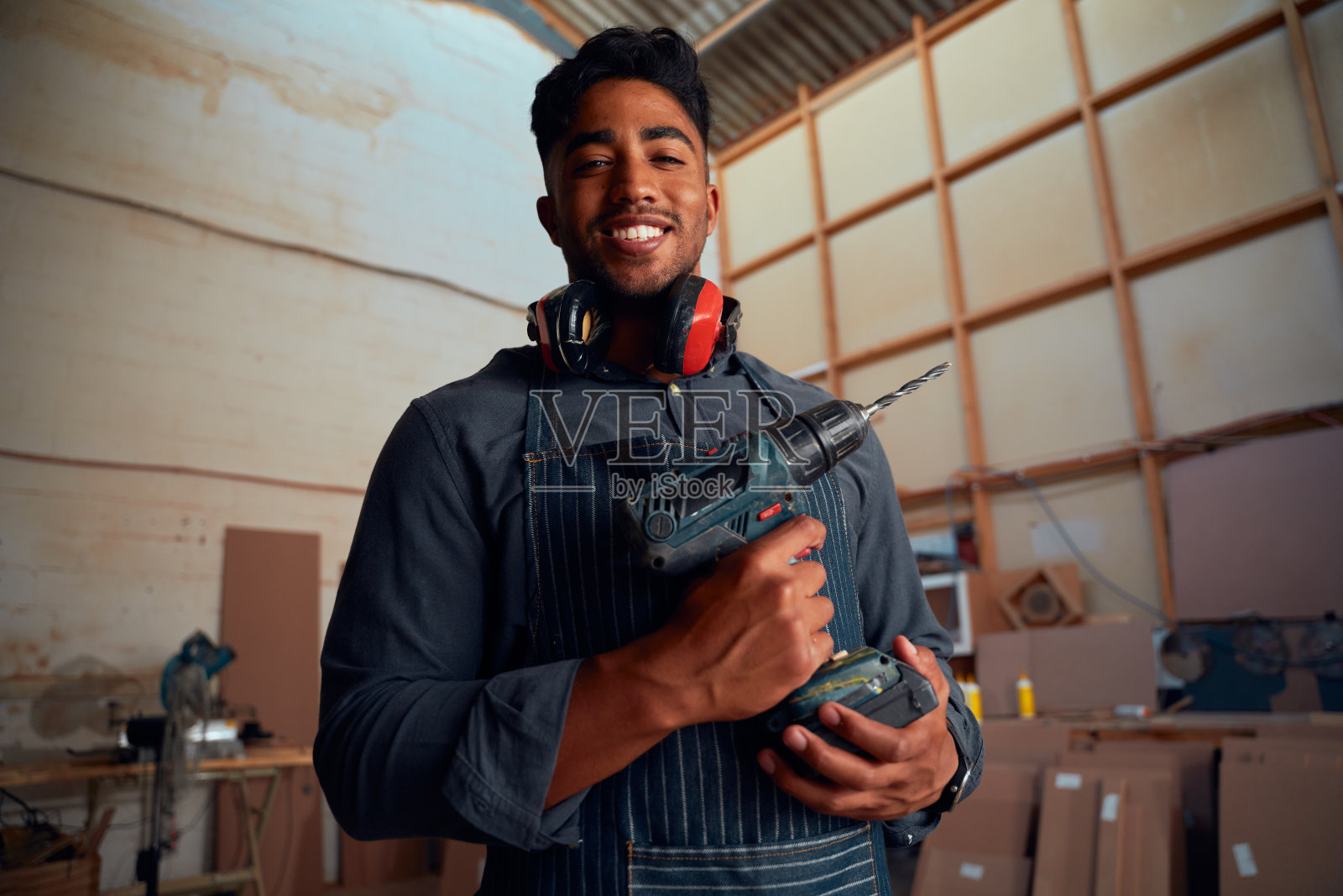 在木工工厂，一个年轻人拿着钻头，面带微笑地看着相机照片摄影图片