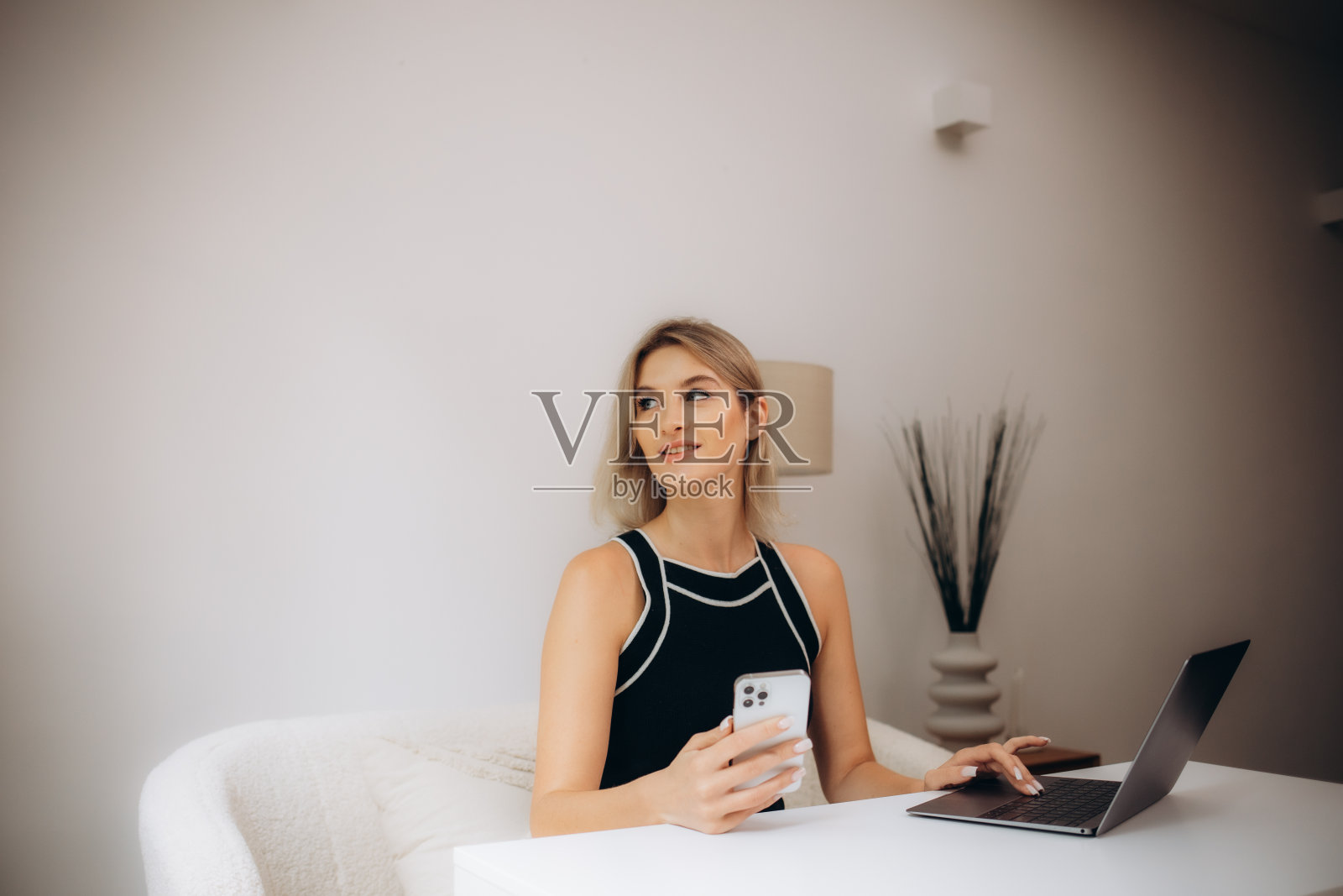 可爱的年轻女士的照片拿着电话，看屏幕，手掌键盘，戴着眼镜，在家里办公室，在室内照片摄影图片