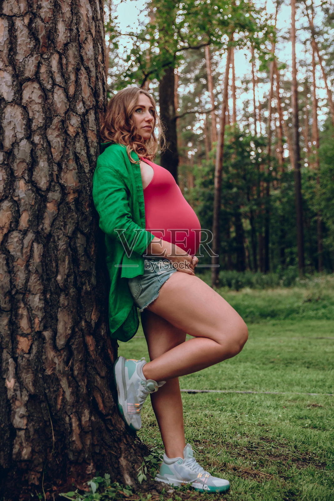 美丽的孕妇倚着树在公园休息照片摄影图片