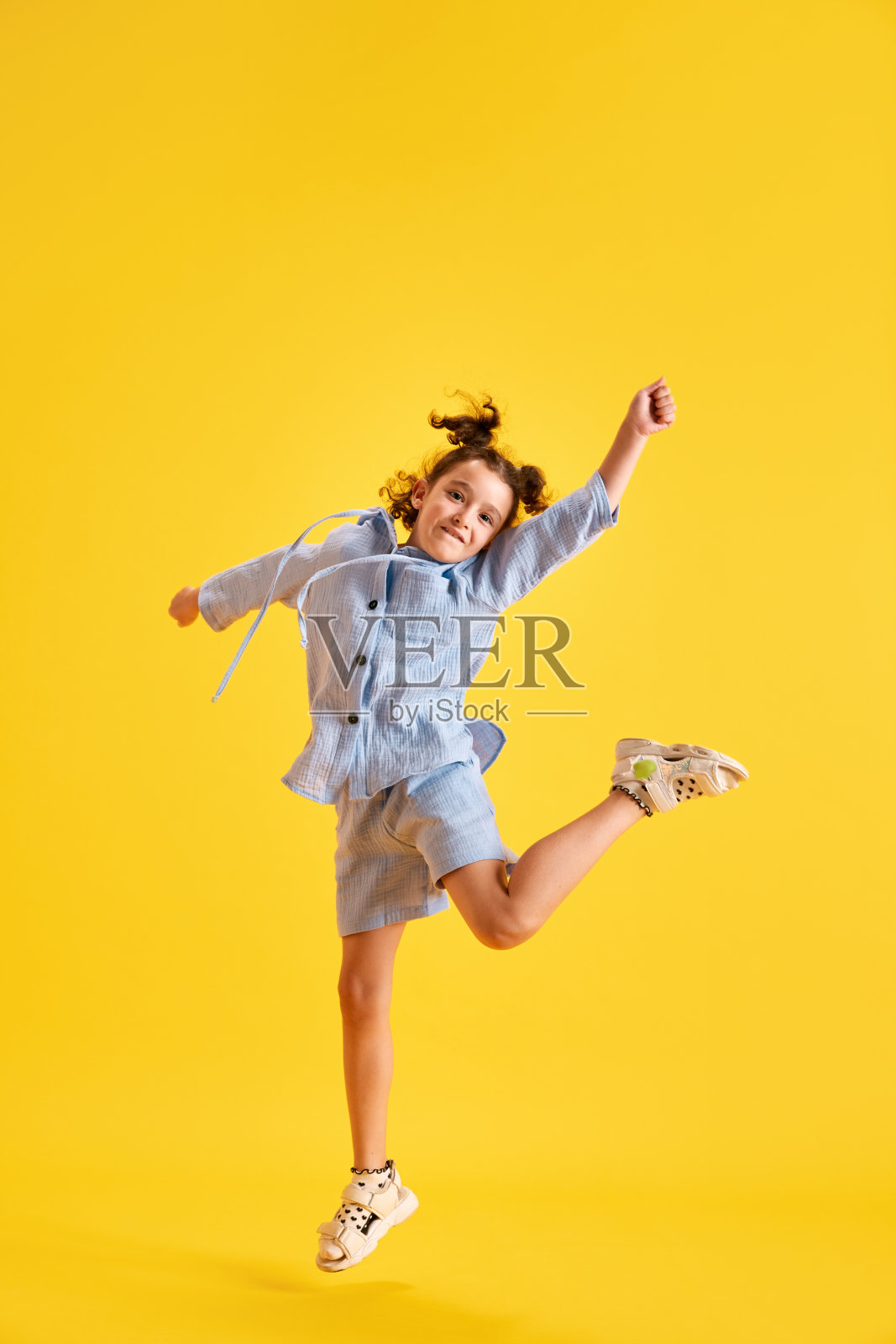 快乐的小女孩的全身画像，孩子穿着休闲服，在黄色的工作室背景下欢快地跳跃照片摄影图片