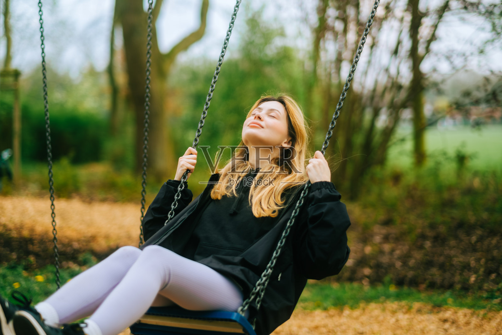 在公园里荡秋千的快乐而年轻的女人。概念的人，没有年龄限制，玩得开心。女性在户外休闲活动中利用秋千享受生活照片摄影图片