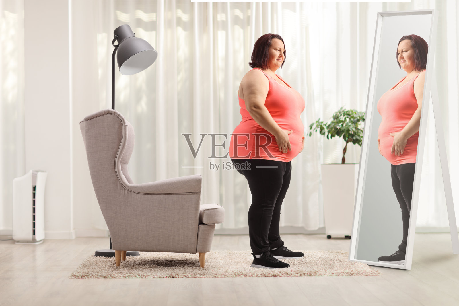 超重的女人在家里对着镜子捂着肚子照片摄影图片