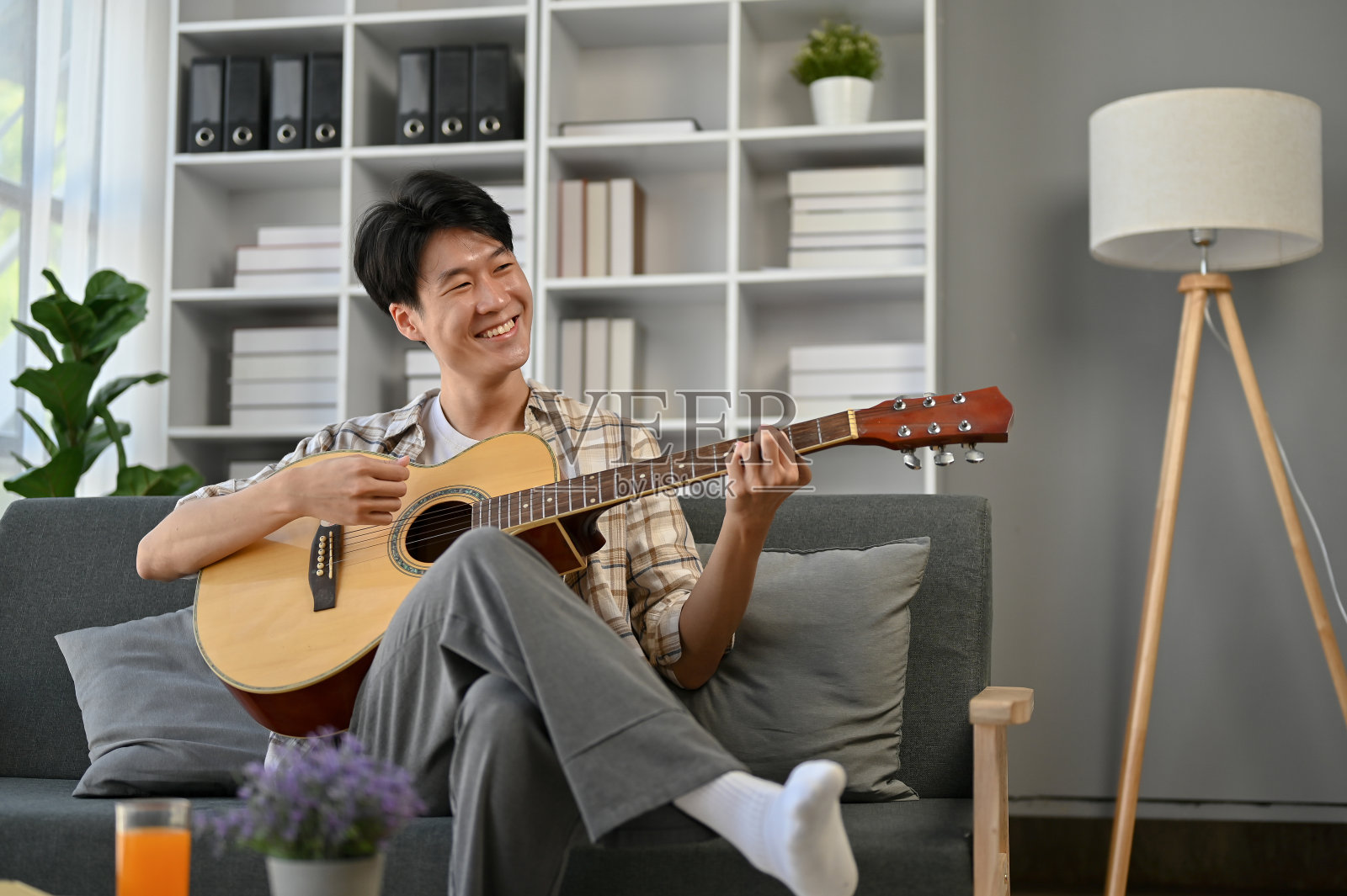 一个开朗的亚洲人坐在客厅的沙发上唱着歌，弹着吉他。照片摄影图片