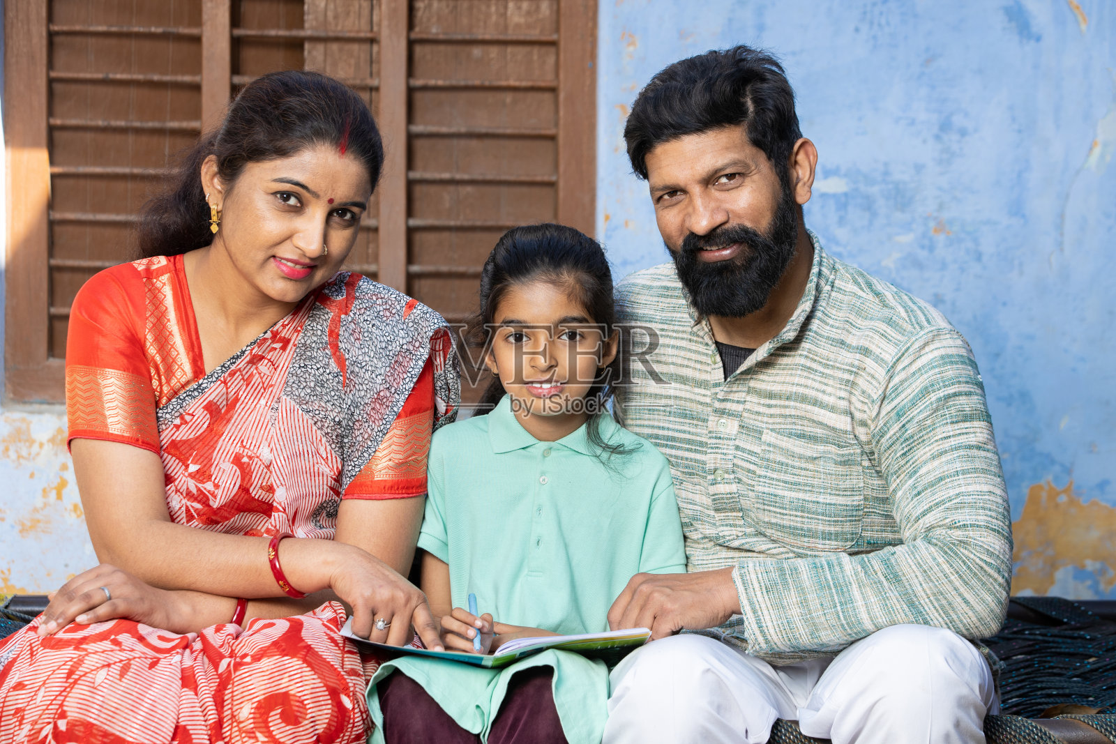 年轻的印度农村父母和孩子坐在一起，手里拿着书看着相机，快乐的农民家庭，教育理念。照片摄影图片