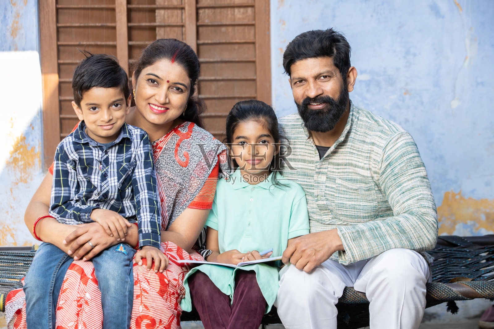 年轻的印度农村家庭坐在镜头前，快乐的农民家庭，父母带着孩子。照片摄影图片