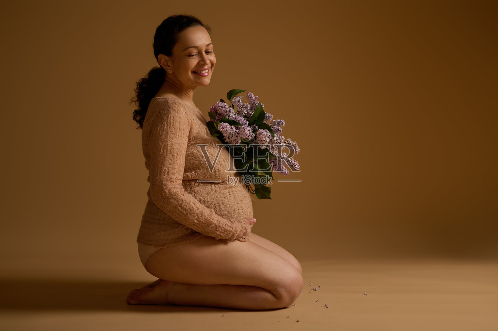 漂亮的孕妇穿着优雅的衣服，坐在米黄色的背景上，抱着肚子照片摄影图片