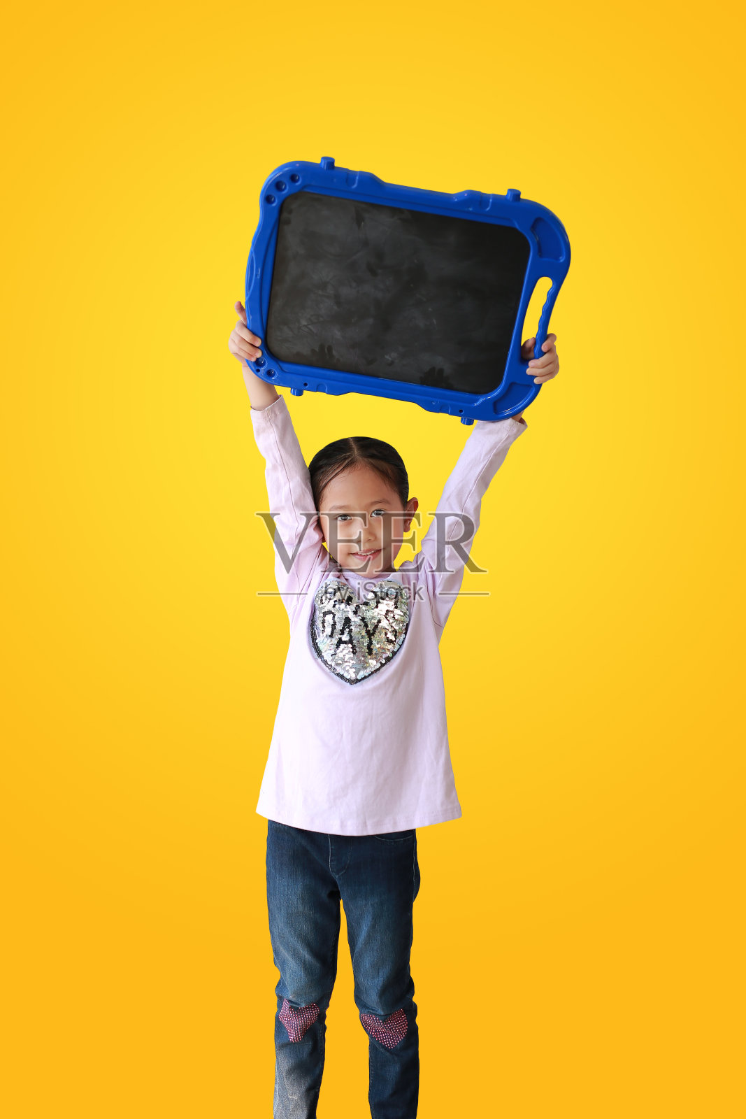 亚洲小女孩拿着黄色背景上的空白黑板。孩子展示空黑板。教育的概念。照片摄影图片