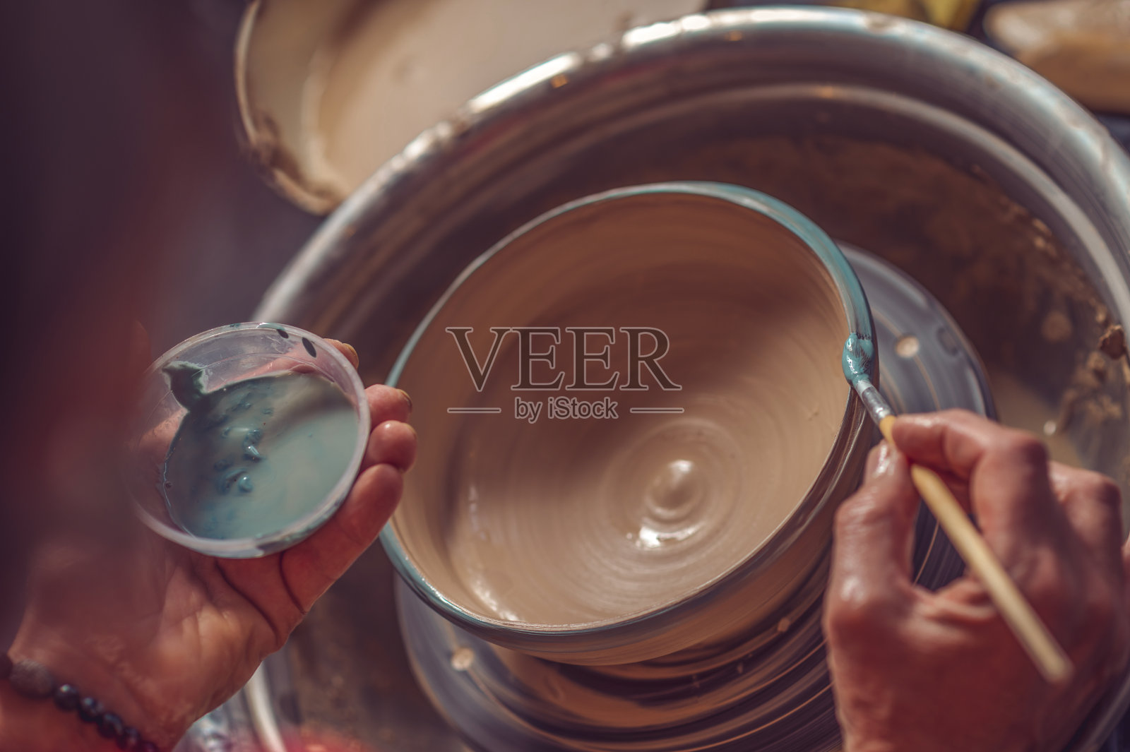 一个妇女在车间里用画笔给陶罐上色。照片摄影图片