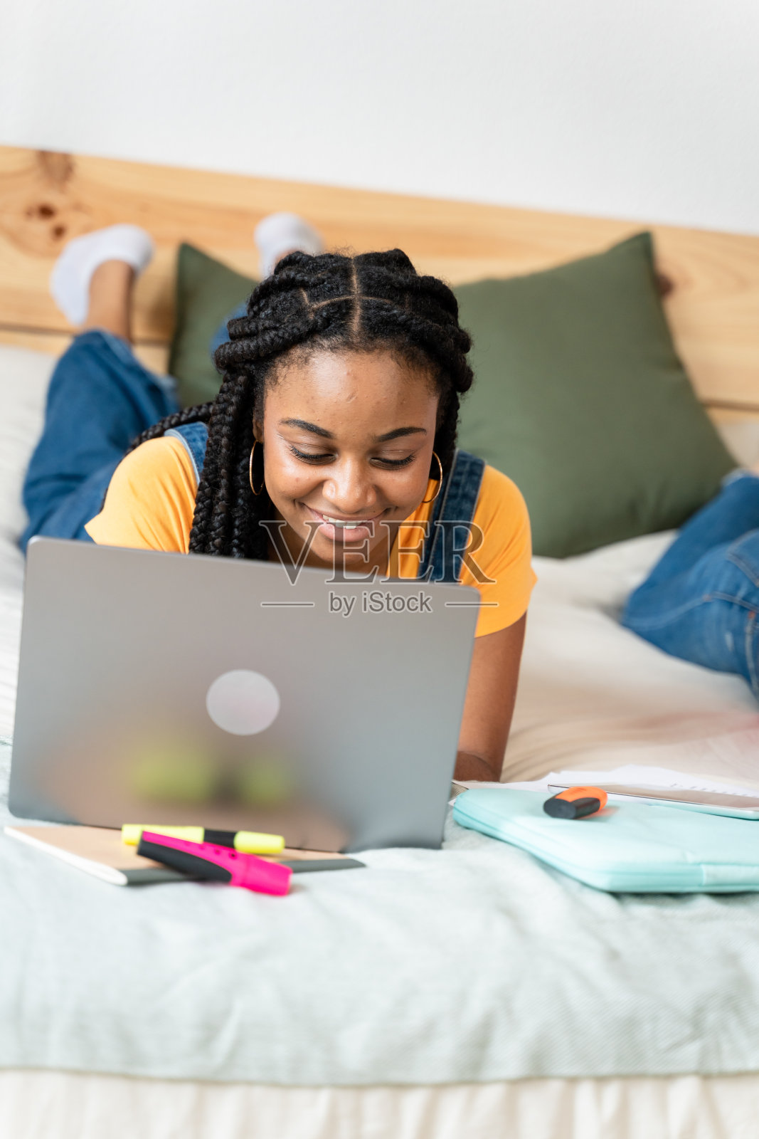 非裔美国女人拿着笔记本电脑躺在床上。照片摄影图片
