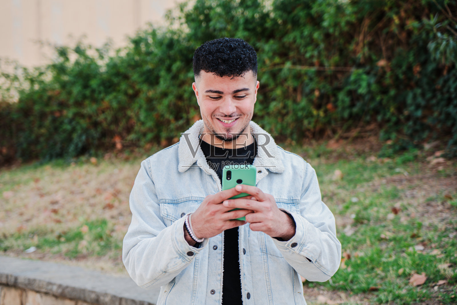 一个面带微笑的摩洛哥人正在用智能手机玩电子游戏。快乐的青少年用手机在社交媒体应用程序上发短信。拿着手机的年轻男性。照片摄影图片