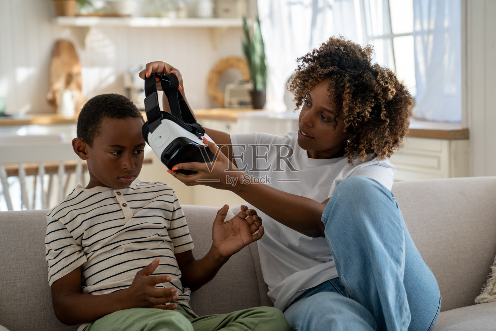 一位非裔美国母亲带着儿子坐在沙发上，摘下了他的虚拟现实眼镜，限制了看屏幕的时间照片摄影图片