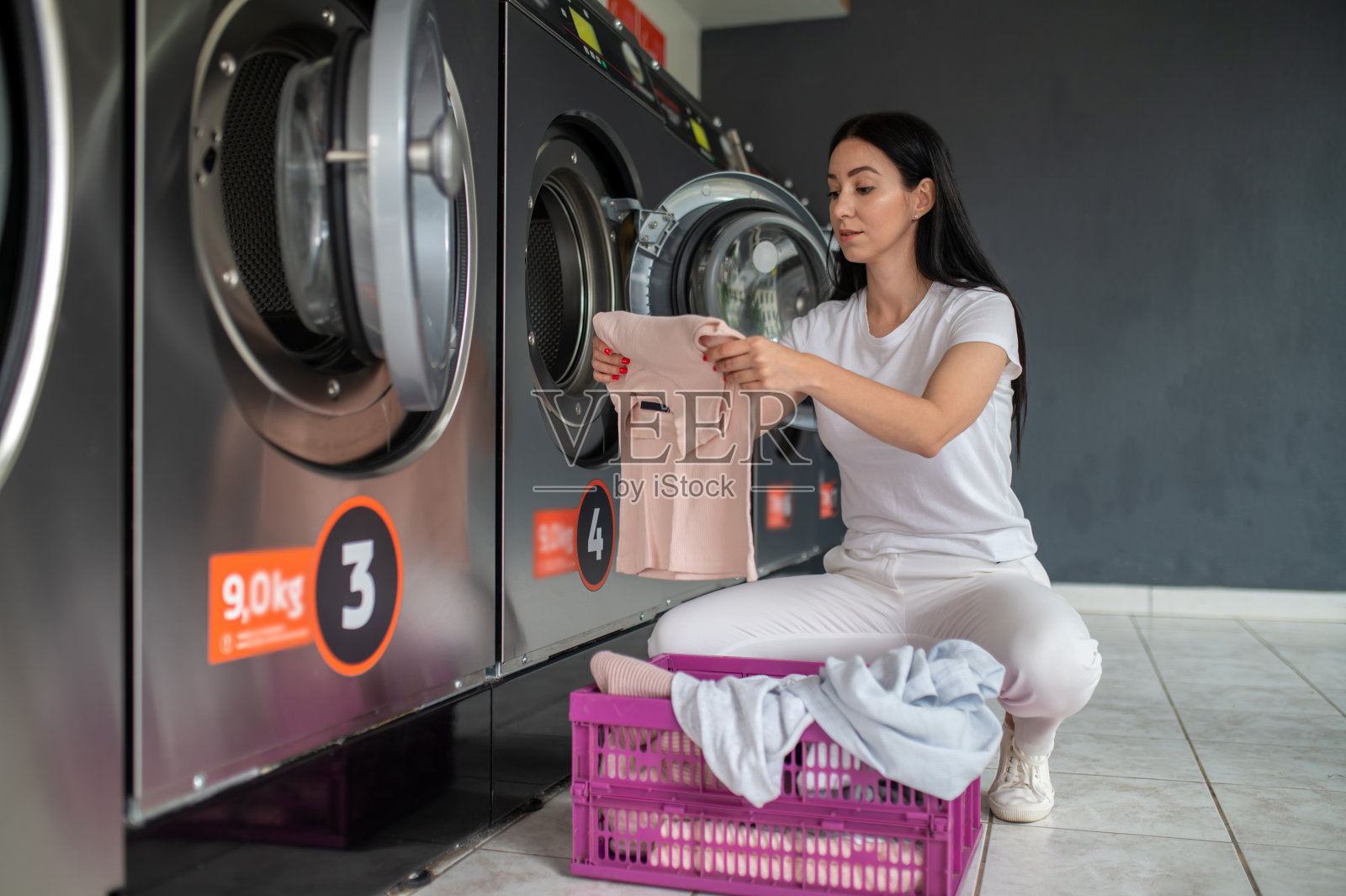 妇女在公共房间使用合格的洗衣机洗衣服。照片摄影图片