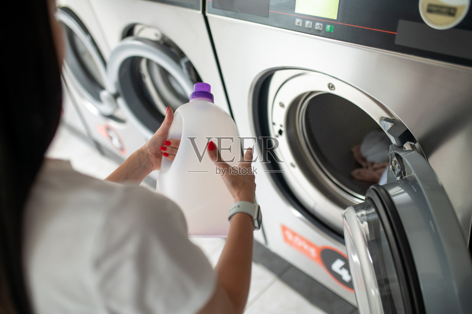 年轻女子拿着洗衣粉使用洗衣机。照片摄影图片