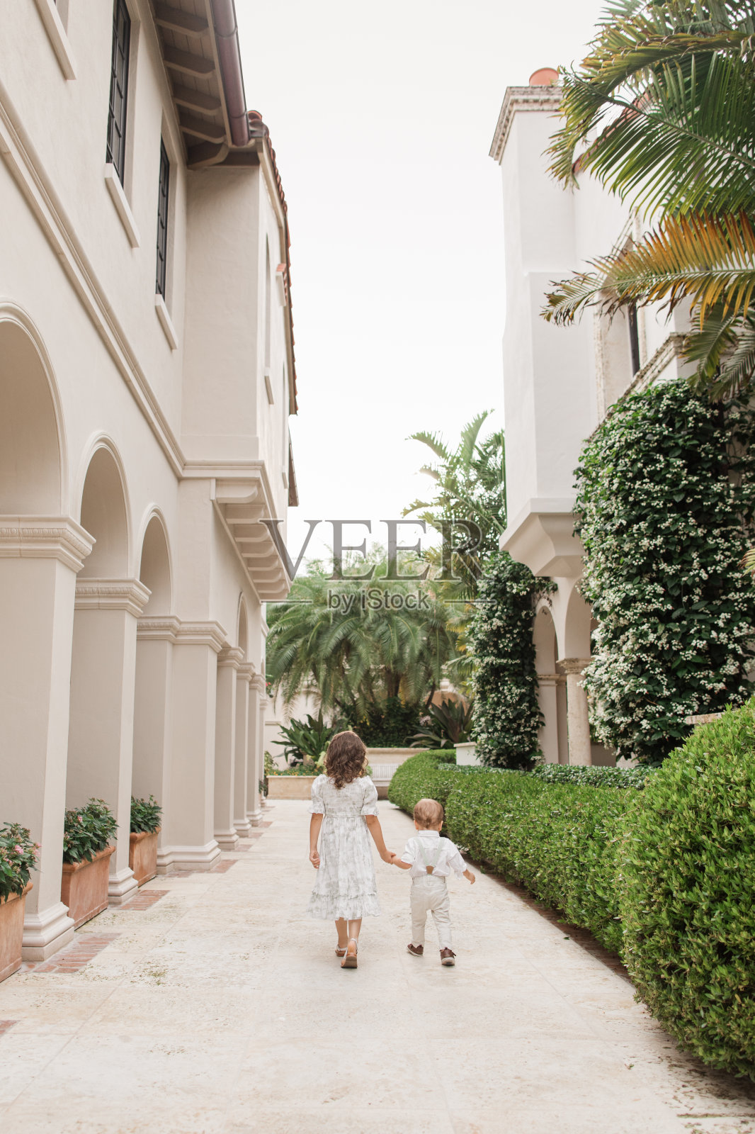 2023年5月，在佛罗里达州棕榈滩，一对兄弟姐妹穿着鼠尾草绿和白色的春装手牵手走在一起，古巴裔美国人4岁的幼女和1岁的男婴都有浅棕色的头发照片摄影图片