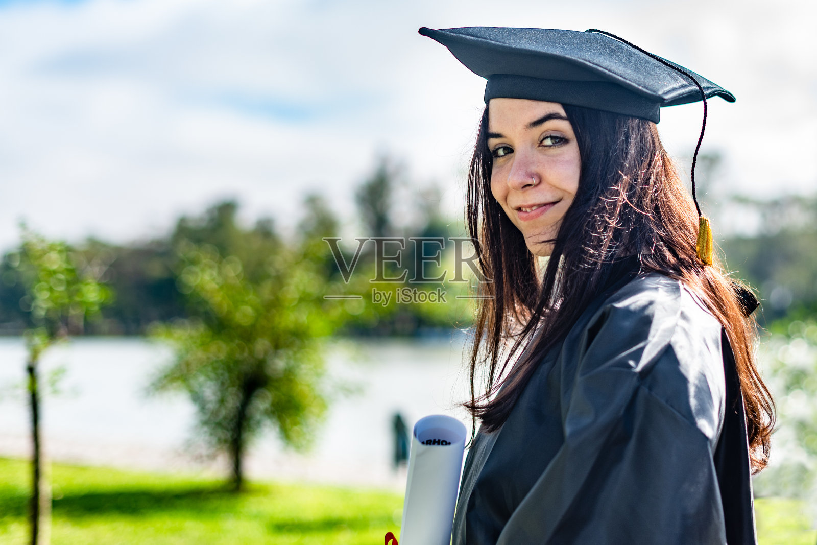 快乐的白人毕业女孩与棕色长发，拿着文凭，看着相机照片摄影图片