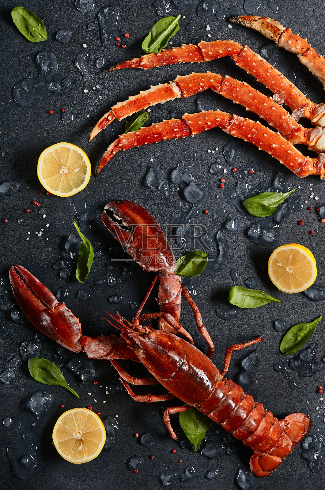龙虾和螃蟹腿，冰和柠檬在黑暗的背景俯视图。熟食螃蟹和龙虾海鲜在黑色石板桌。甲壳类的海鲜美学。奢侈的食物——活龙虾和蟹腿。照片摄影图片
