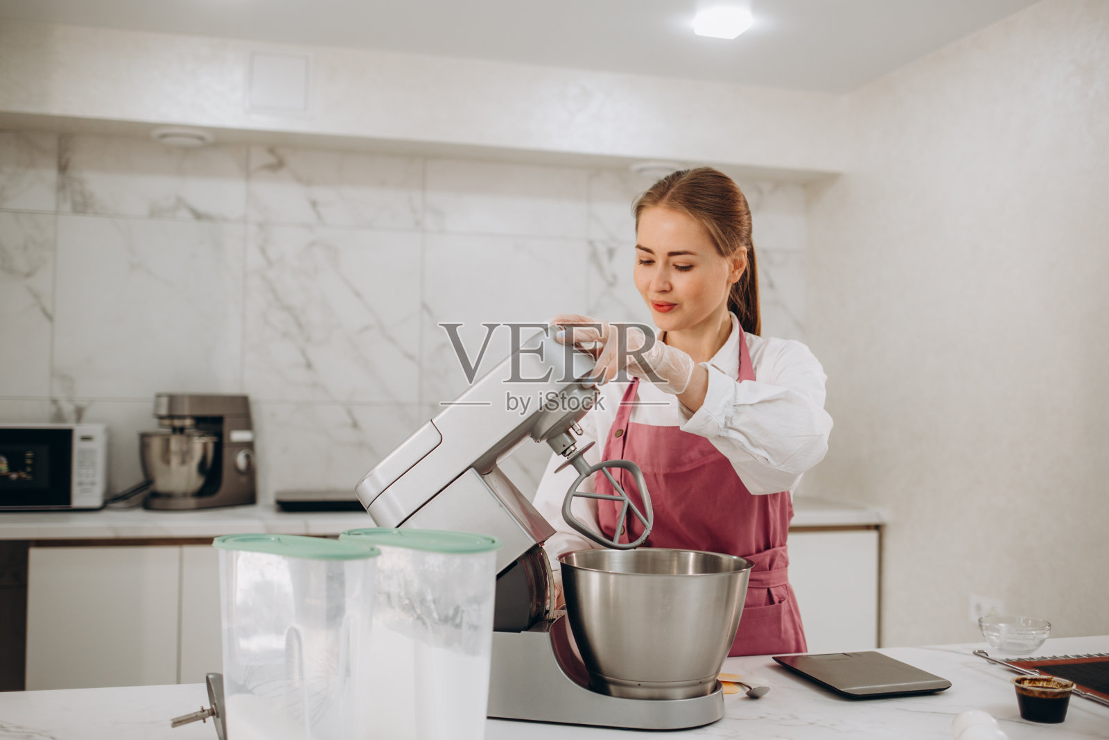 站在现代厨房里，年轻女子用搅拌器搅拌奶油做蛋糕。照片摄影图片