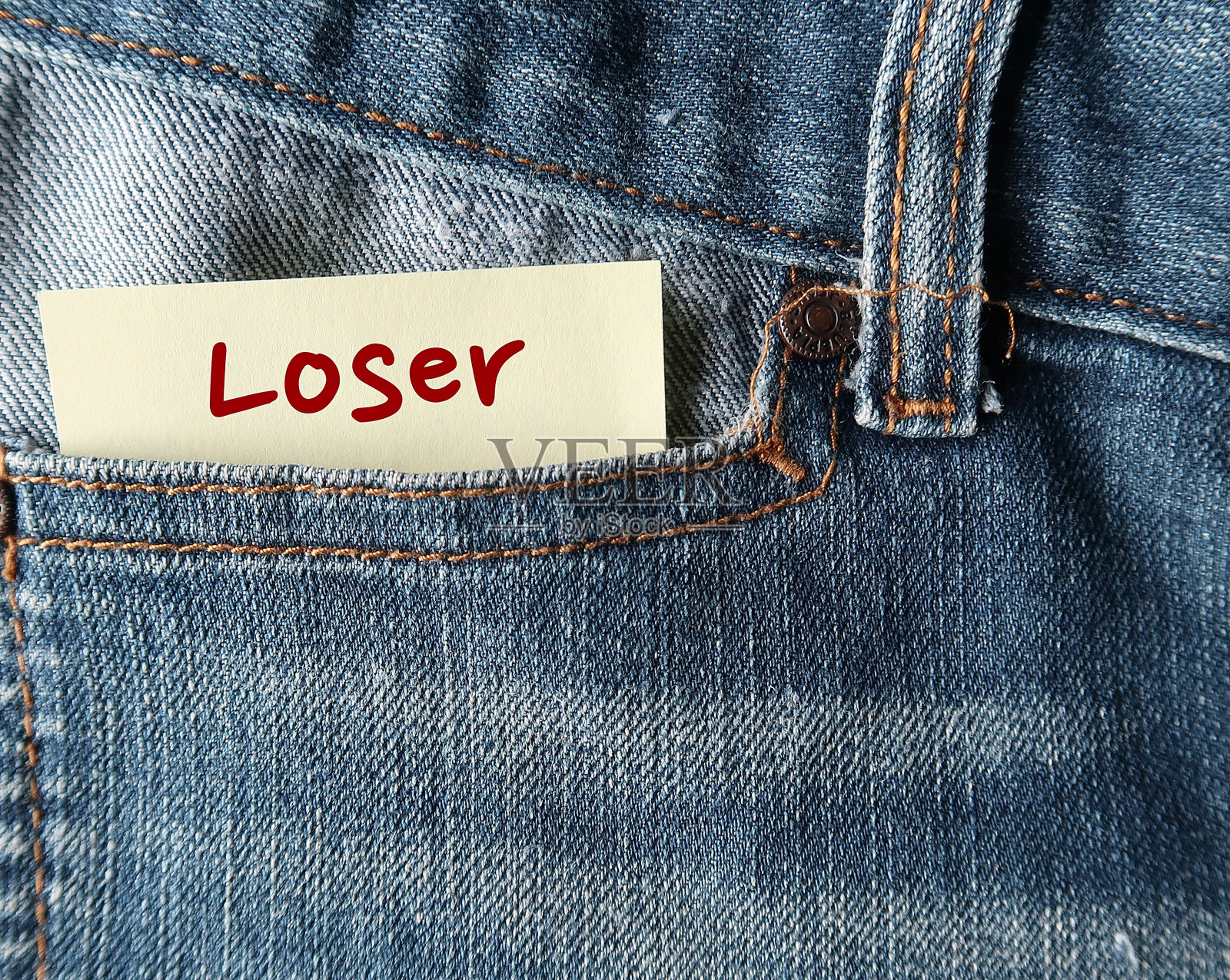 牛仔裤口袋里的黄色纸条上写着“失败者”，指的是一个总是失败、被打败或凡事不成功的人——这可以变成一个奋斗并取得胜利的人照片摄影图片
