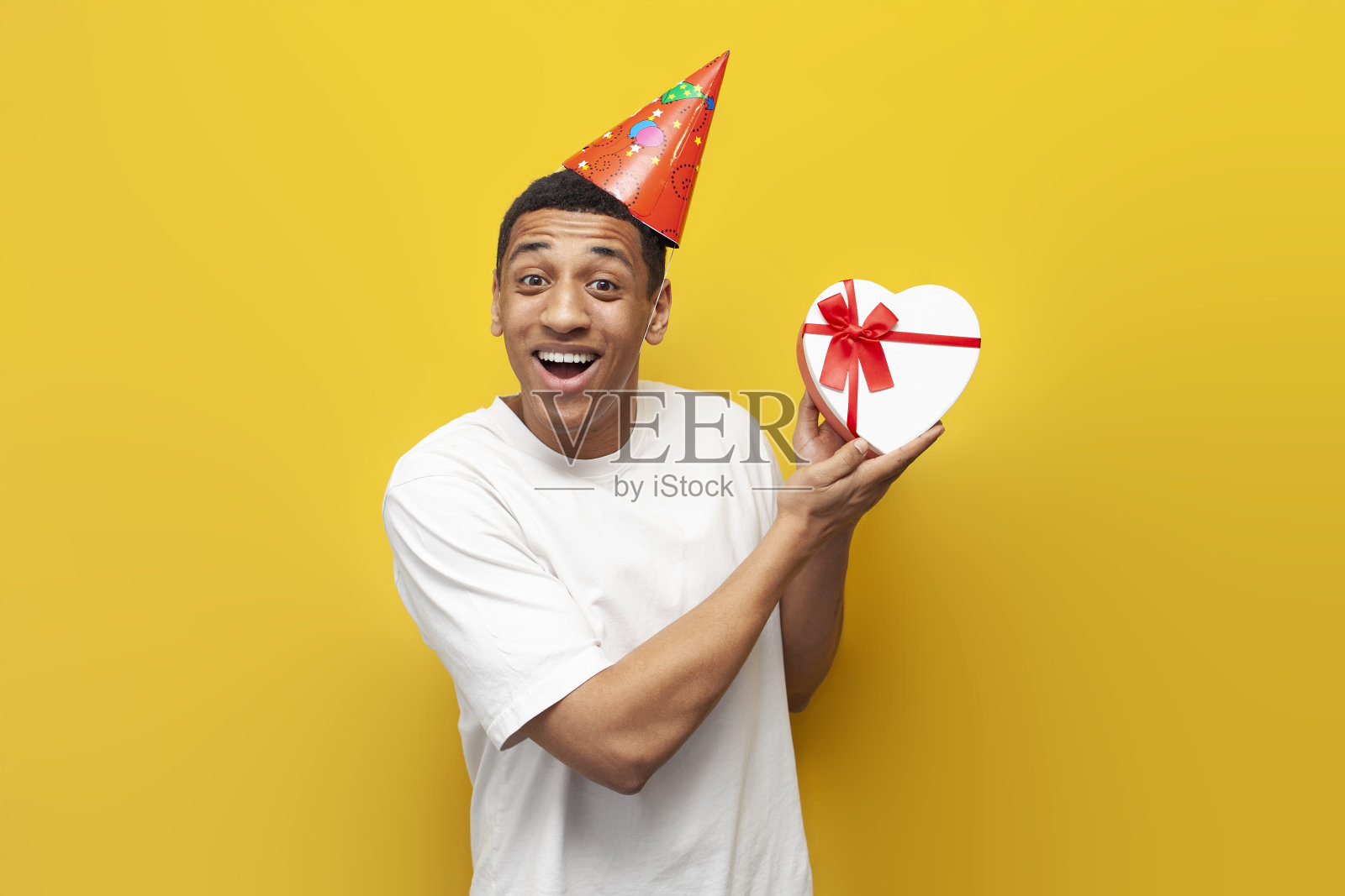 快乐的非洲裔美国人戴着派对帽庆祝生日，手里拿着心形的礼盒照片摄影图片