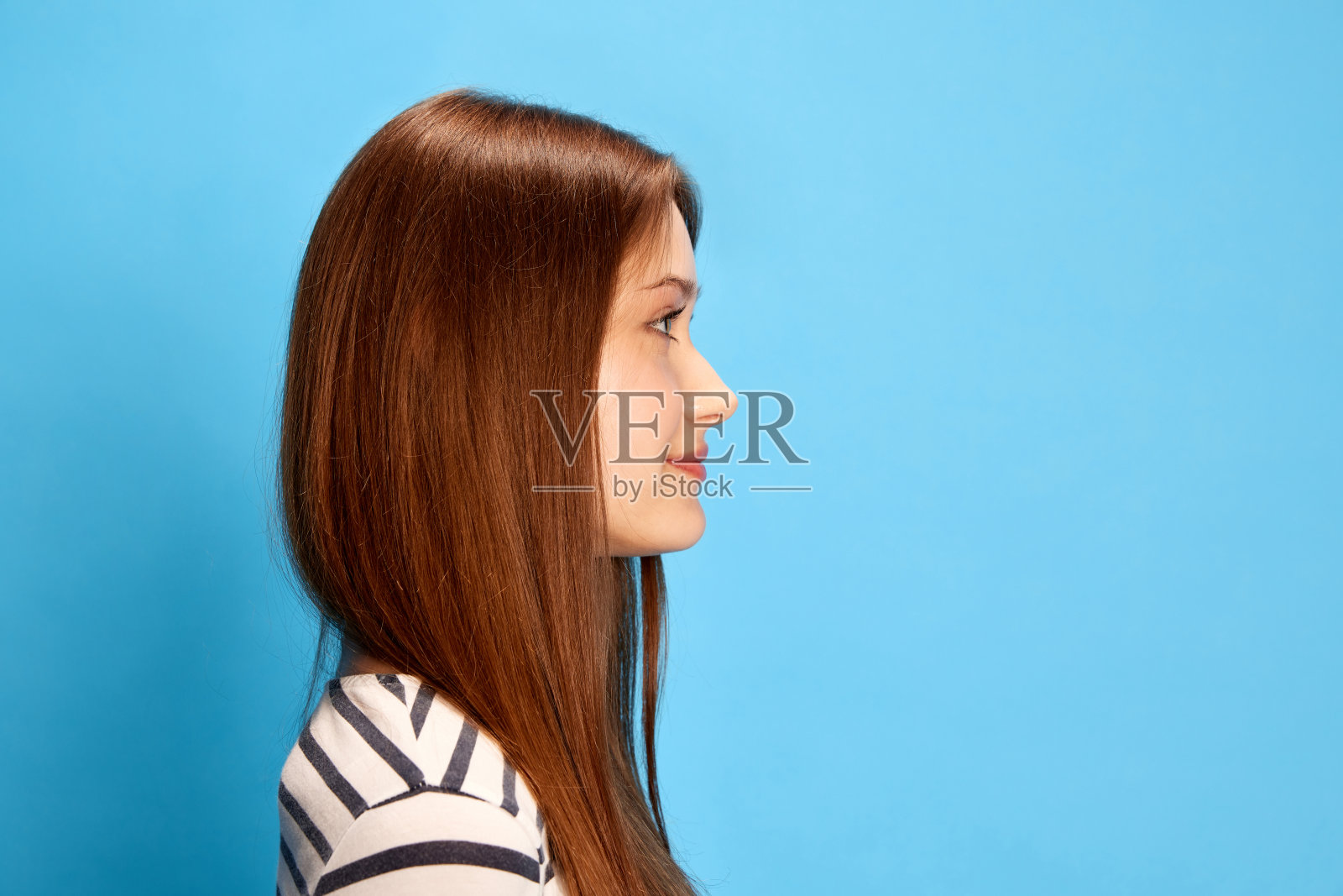 侧视图的年轻女孩直发向前看，在蓝色工作室的背景下摆姿势照片摄影图片