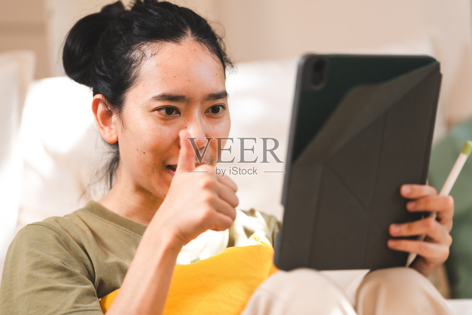 年轻的亚洲女人在客厅用数码平板电脑视频通话，微笑的年轻亚洲女人在家里用数码平板电脑视频聊天，女人在网上聊天时问候某人照片摄影图片