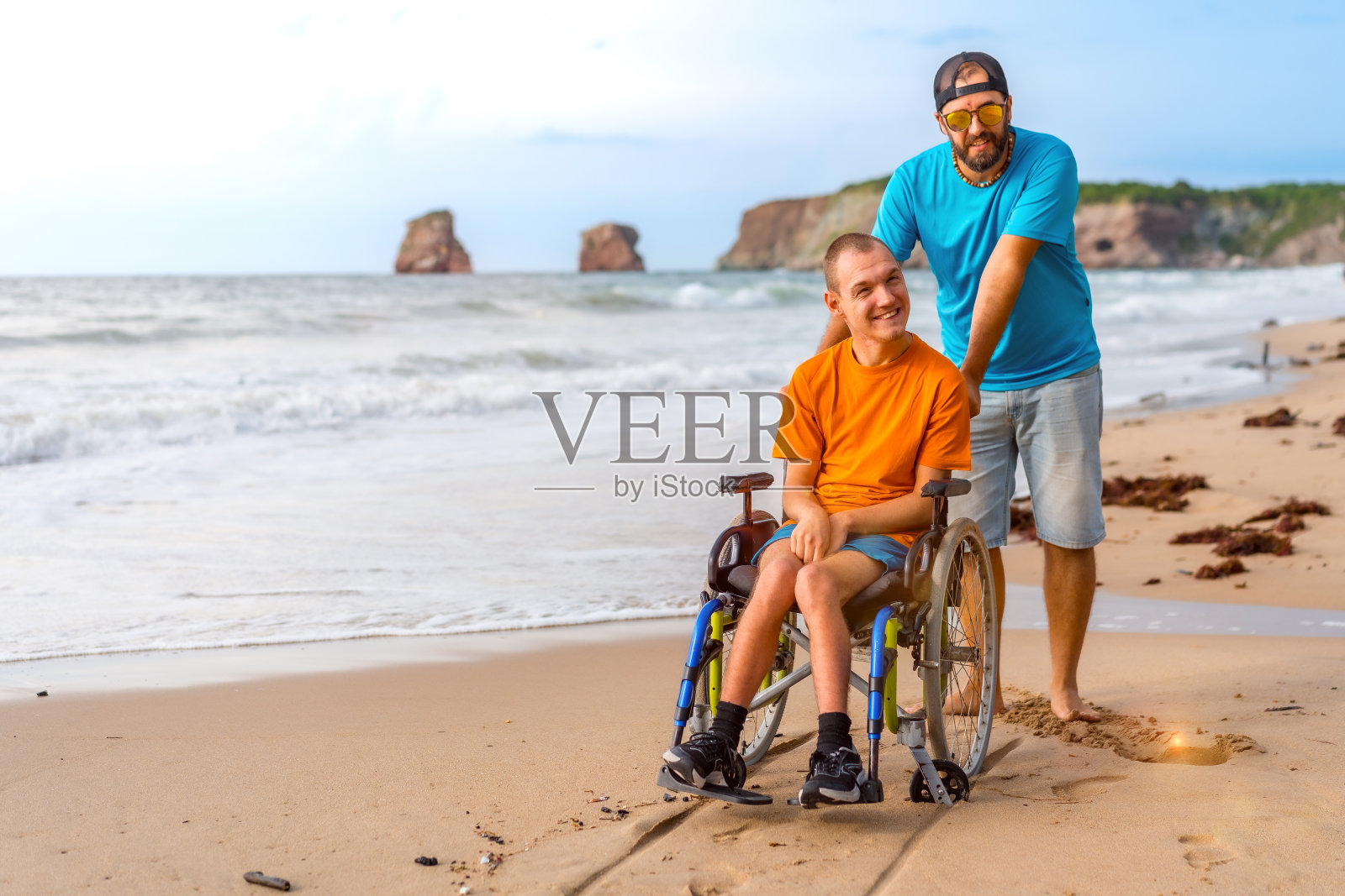 海边的朋友推着一个坐在轮椅上的残疾人照片摄影图片