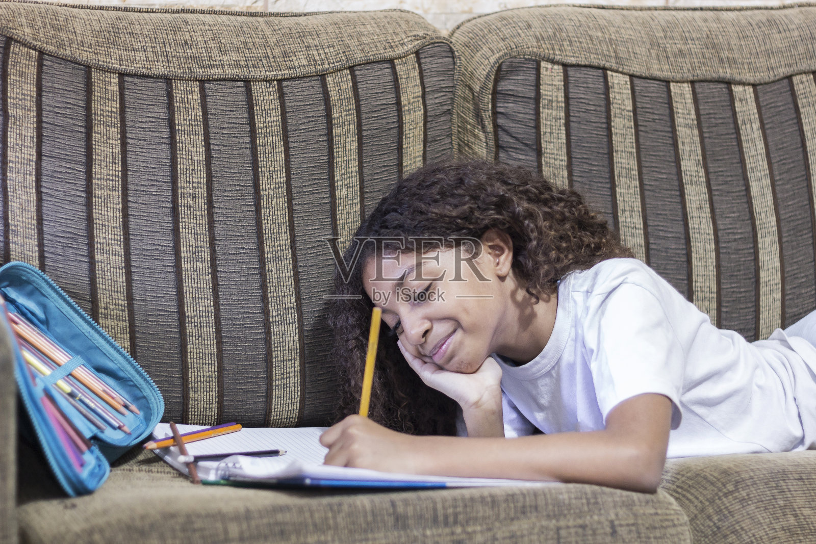 在沙发上做作业，面带微笑，快乐的女学生照片摄影图片