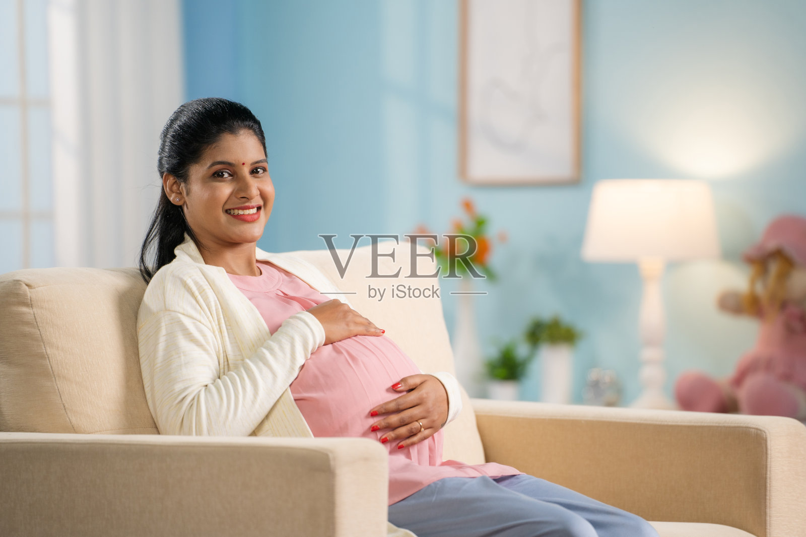 快乐微笑的孕妇通过触摸或感觉肚子看着镜头-期待母亲，产前联系和母性的概念照片摄影图片