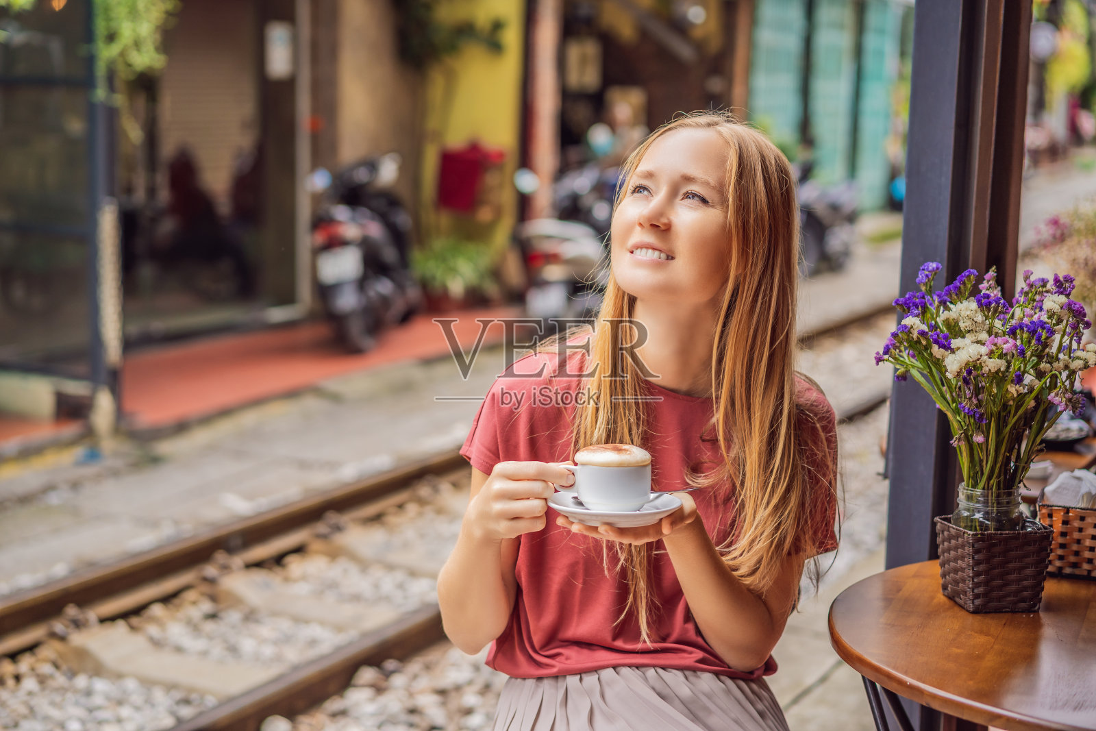 年轻的女游客坐在穿过河内市居民区的铁路旁喝着越南咖啡和鸡蛋。河内火车街是著名的旅游胜地。越南在冠状病毒隔离后重新开放照片摄影图片