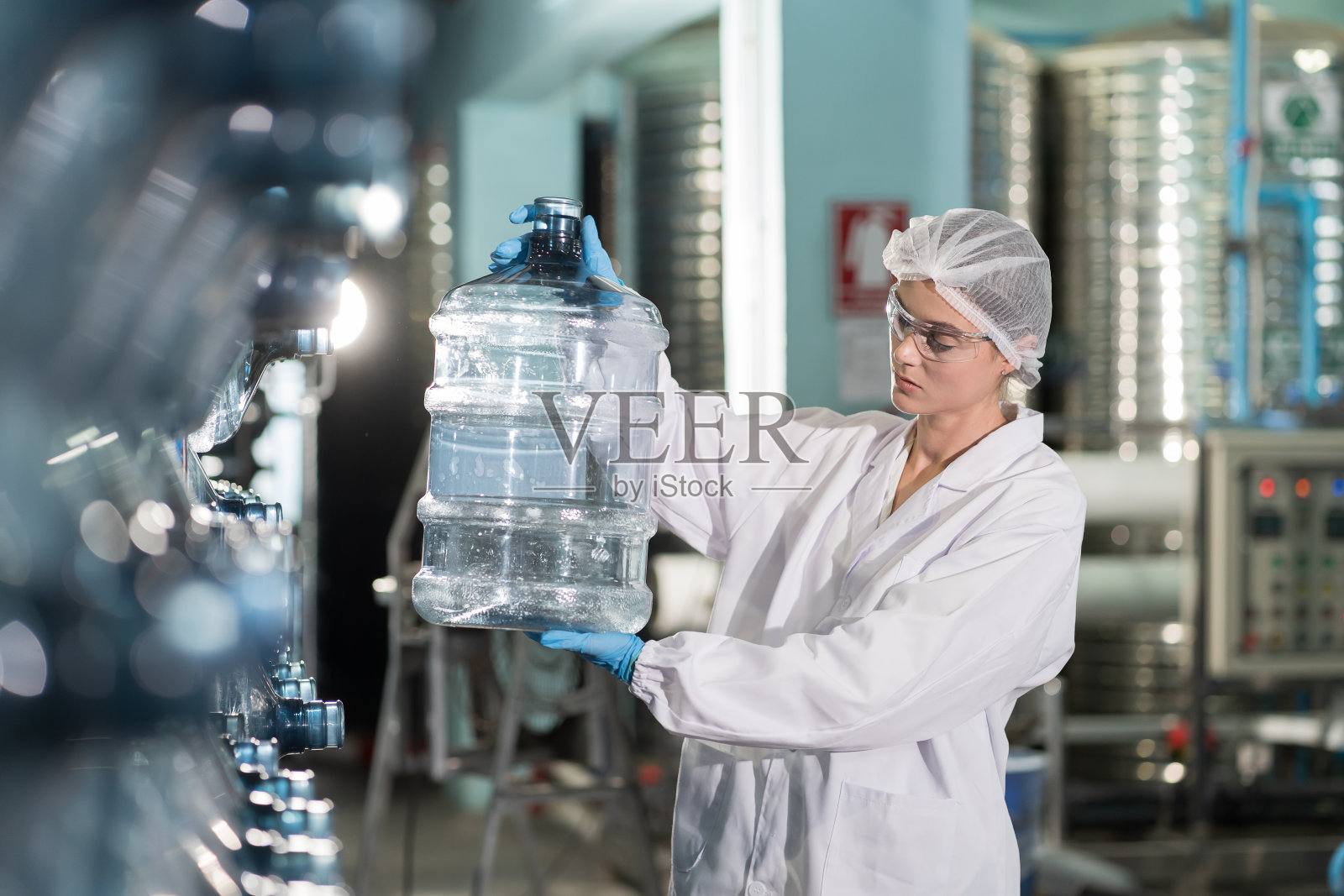 女工在矿泉厂生产塑料饮用水箱质量检测。工厂女工在装瓶过程中检查塑料瓶照片摄影图片