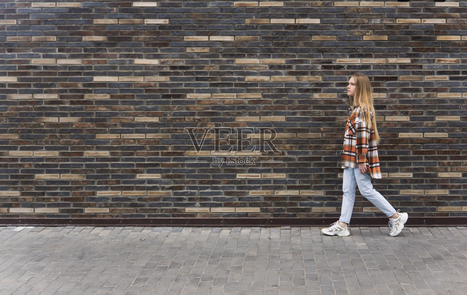 年轻女子靠着砖墙走在街上照片摄影图片