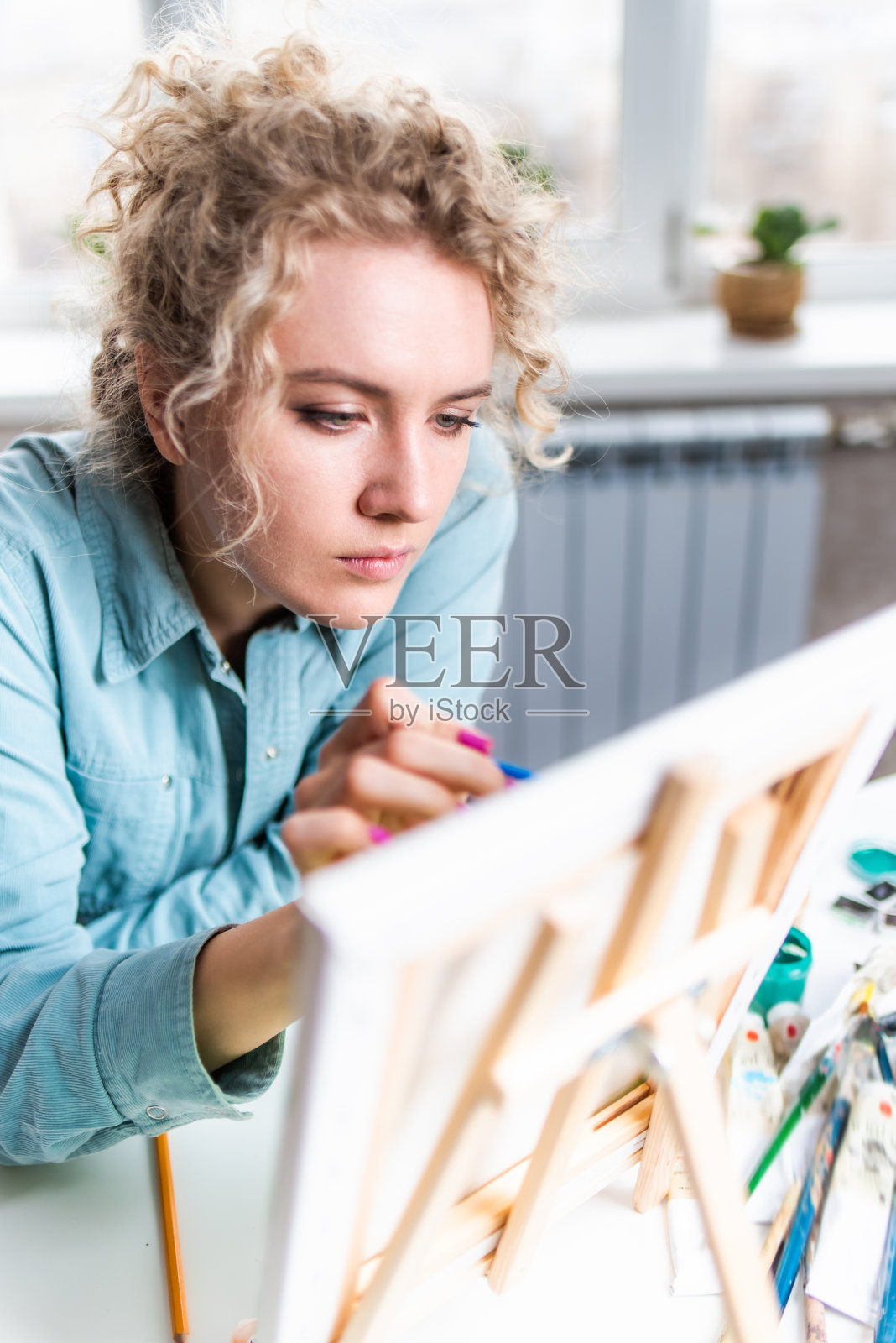 窗边画着画的卷发金发女人照片摄影图片