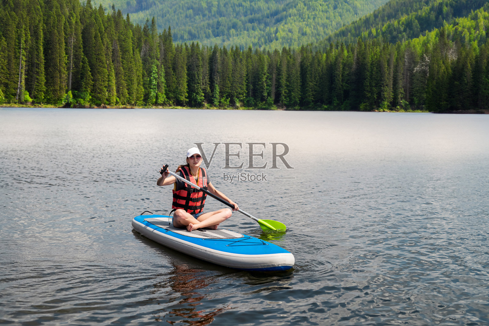 迷人的微笑的女人骑着桨板绕着城市的湖照片摄影图片